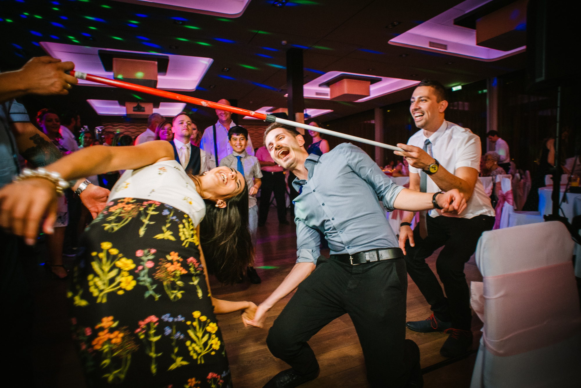 Guests holding hands and dancing during limbo game on lively wedding dance floor.