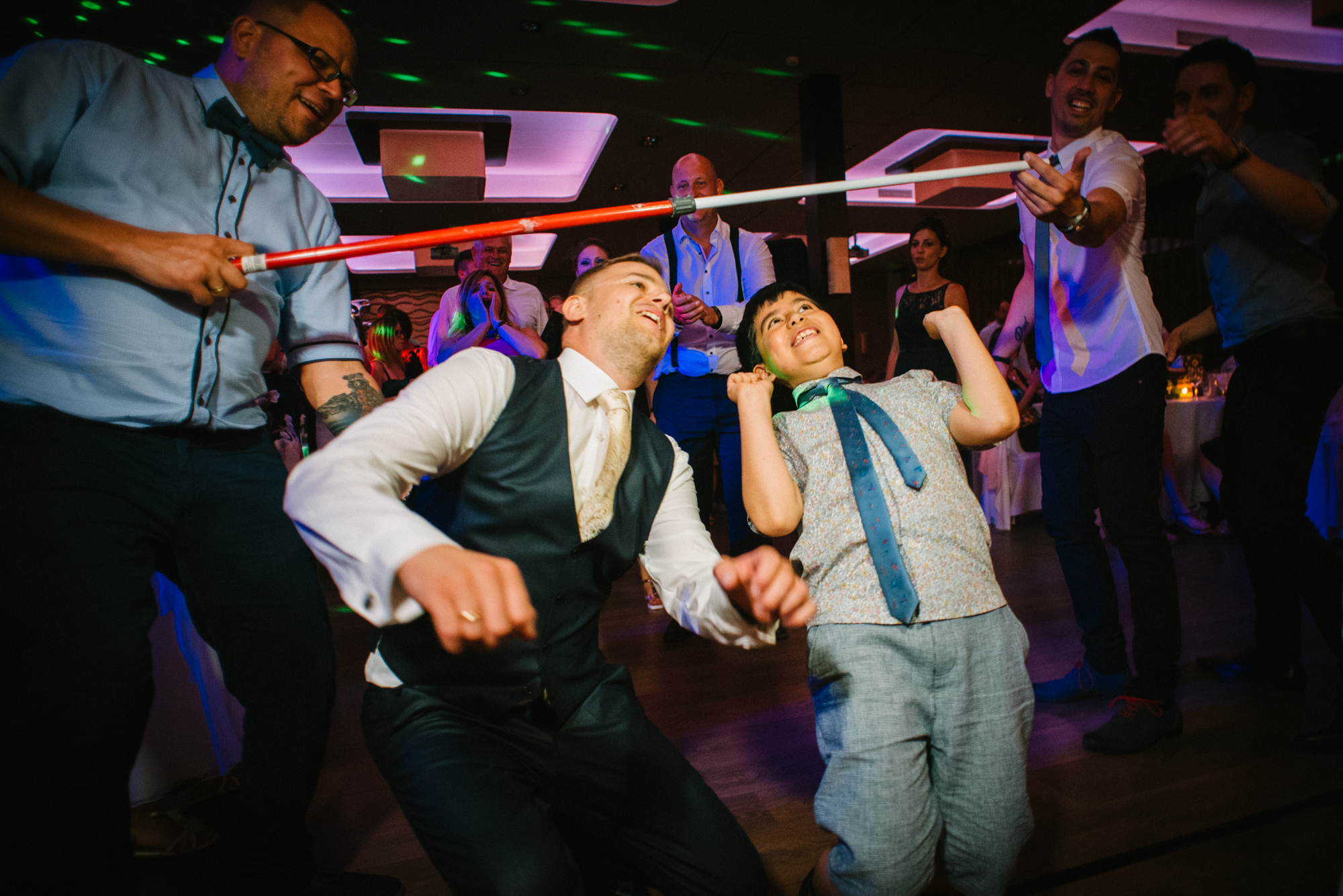 Wedding guests laughing while participating in limbo dance game during evening celebration.
