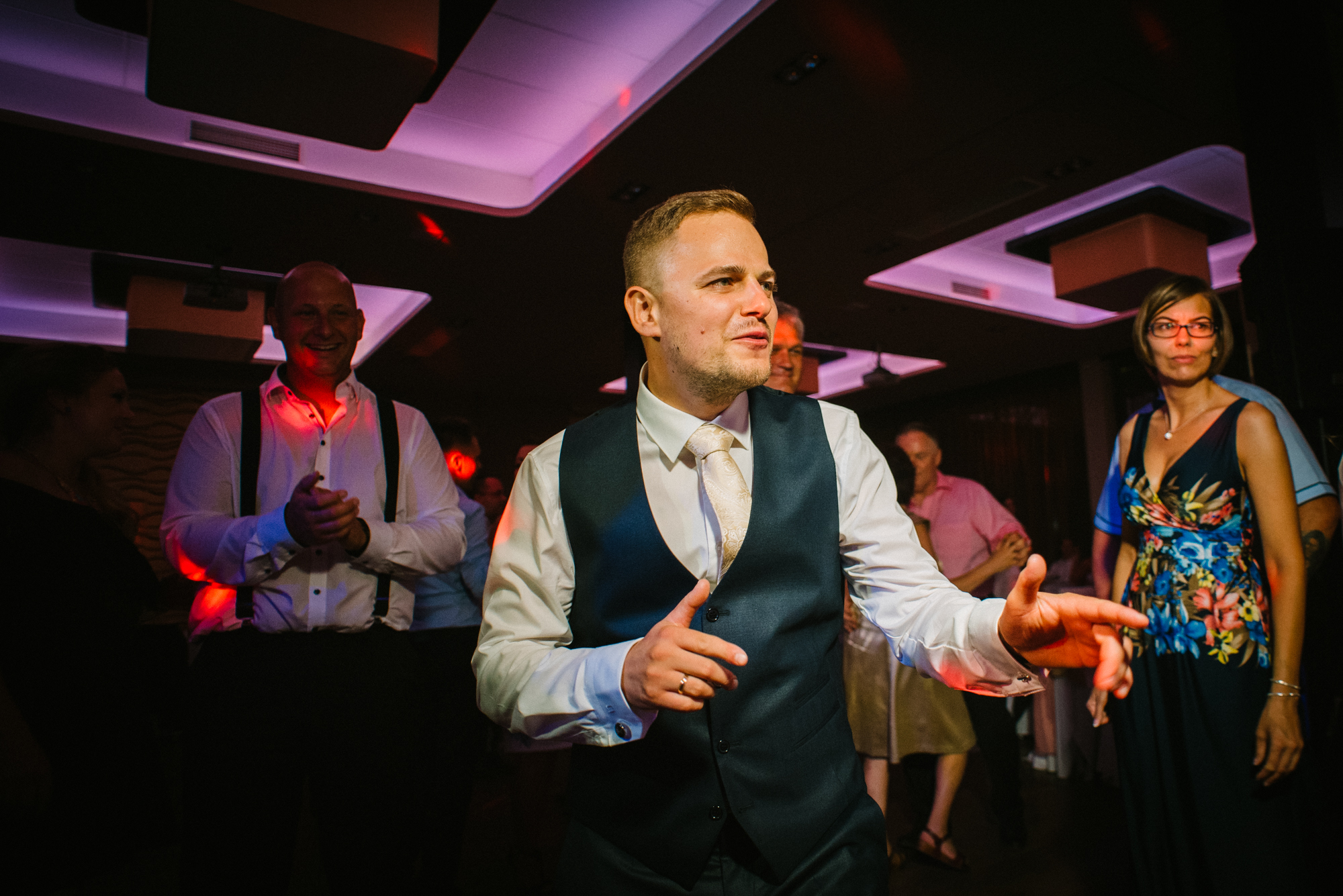 Groom dancing confidently on wedding dance floor surrounded by guests and vibrant lighting.