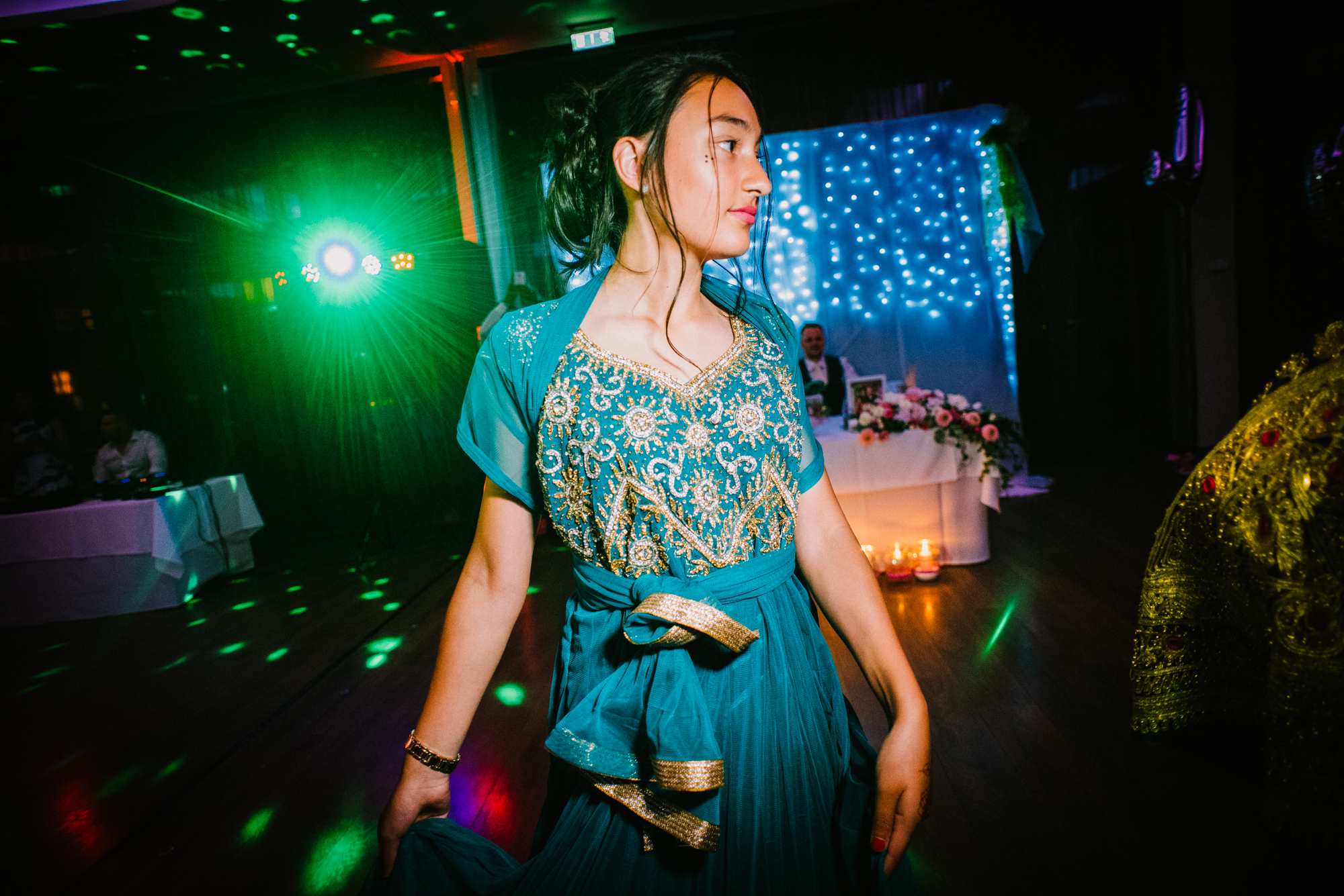 Woman in traditional Afghan dress dancing gracefully under colourful lights at wedding reception.