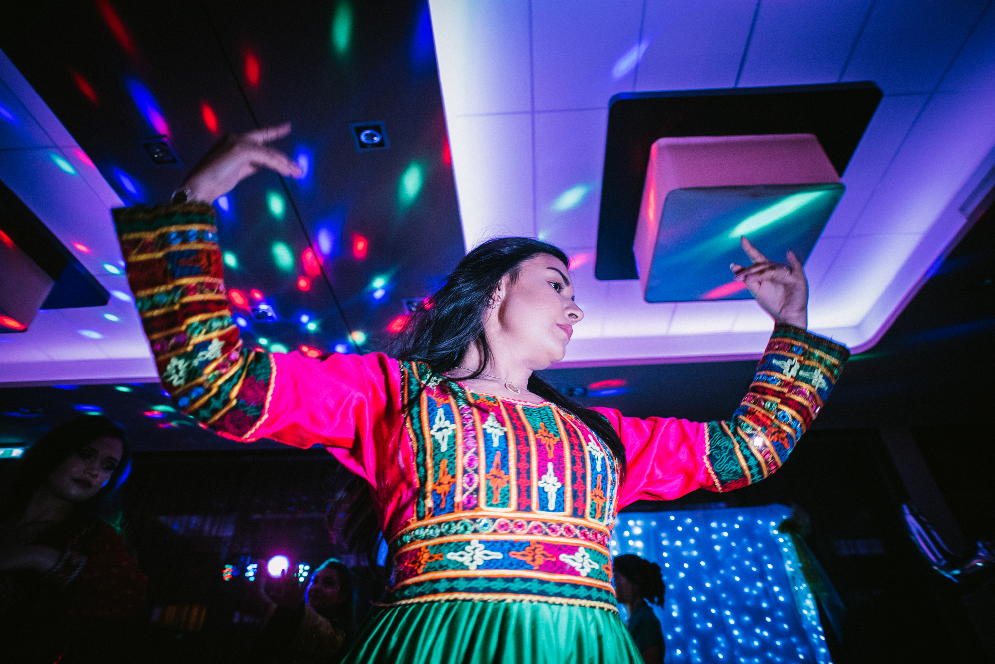 Woman in vibrant cultural outfit dancing on wedding dance floor with dynamic lighting effects.