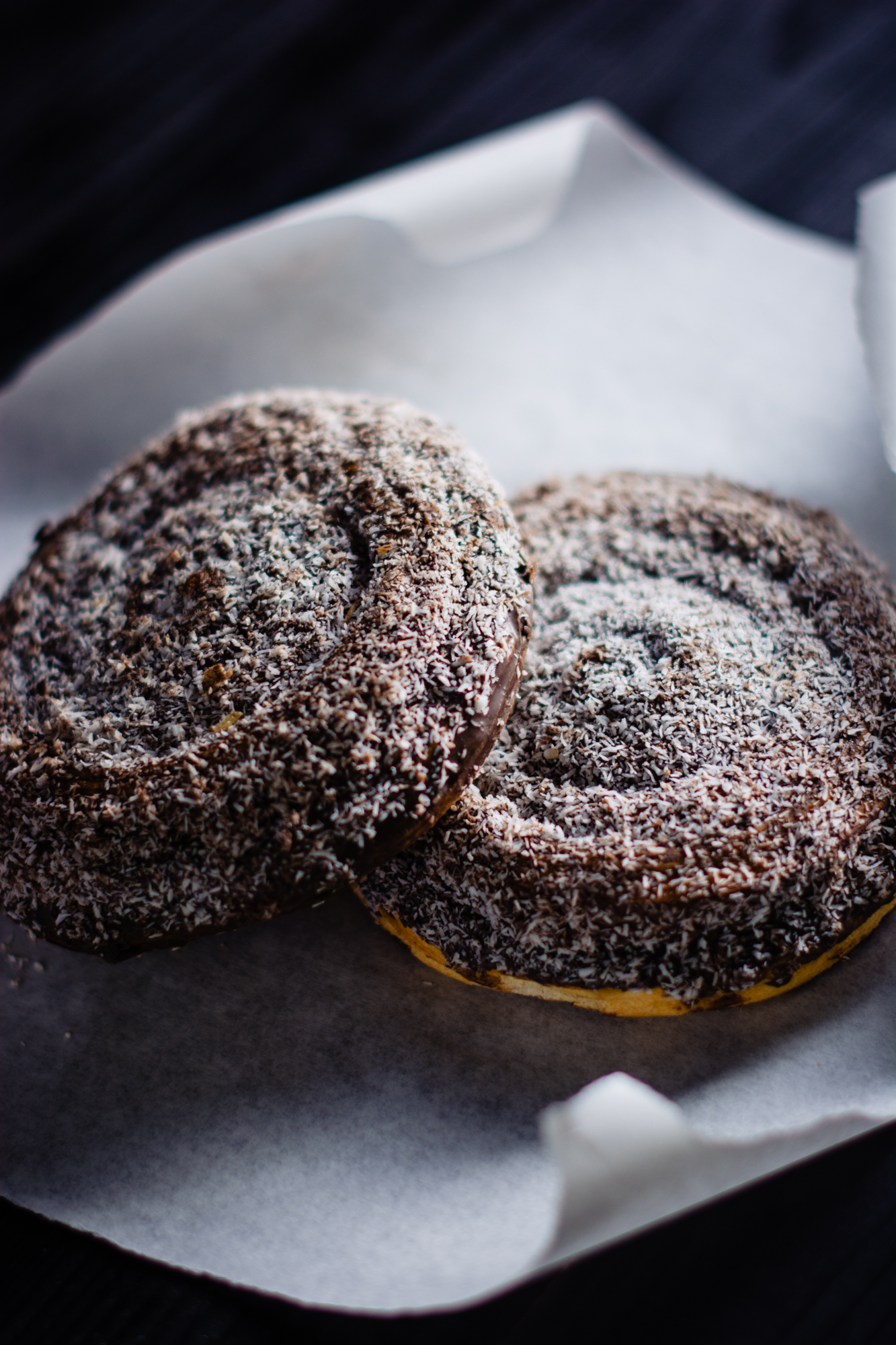 Close-up of coconut-covered pastries with textured chocolate coating on bakery paper.