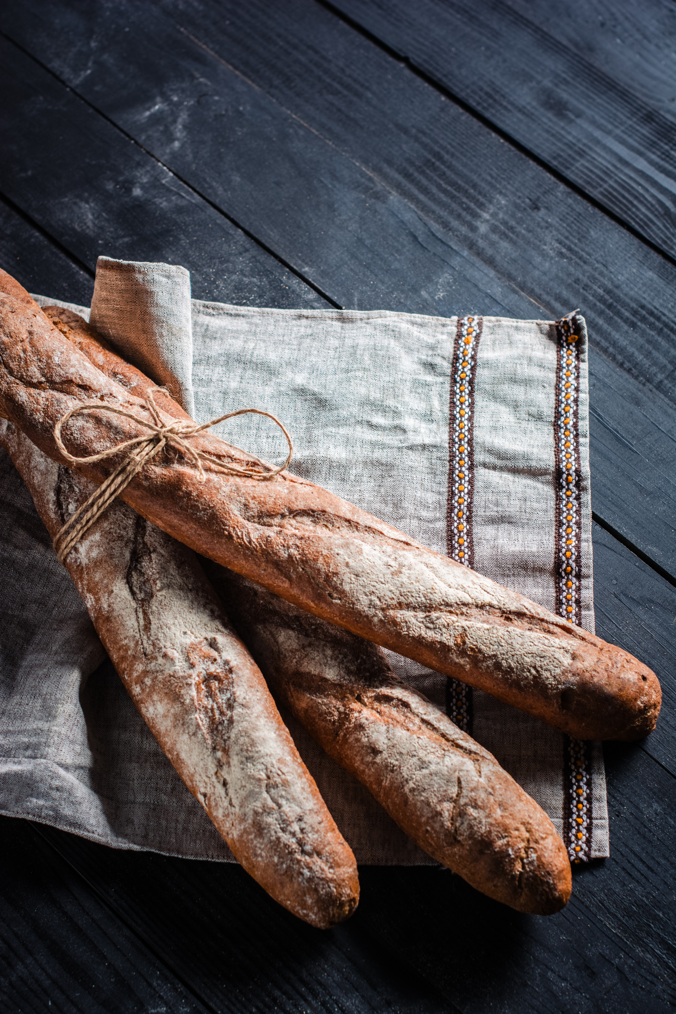 Flour-dusted baguettes tied together on linen cloth, photographed in rustic bakery style.