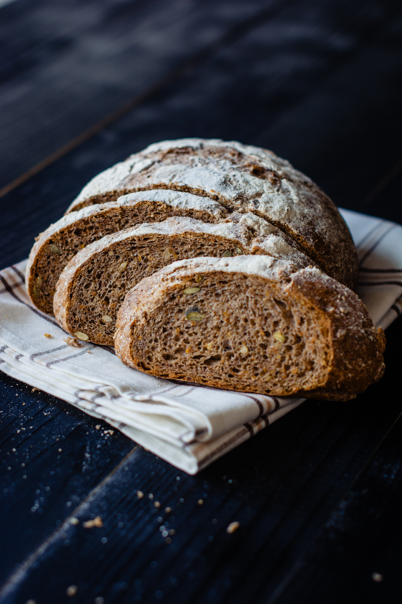 Sliced artisan bread showing soft crumb and seeds, styled on linen in bakery photography.