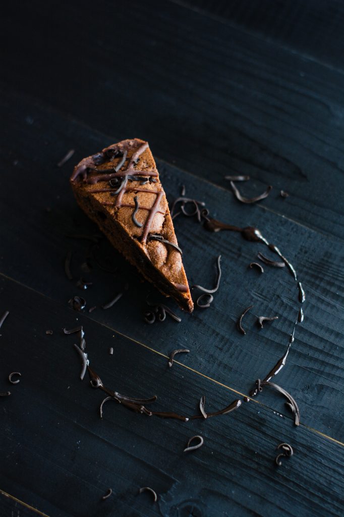 Chocolate cake slice with ganache drizzle and shavings arranged on dark wooden surface.