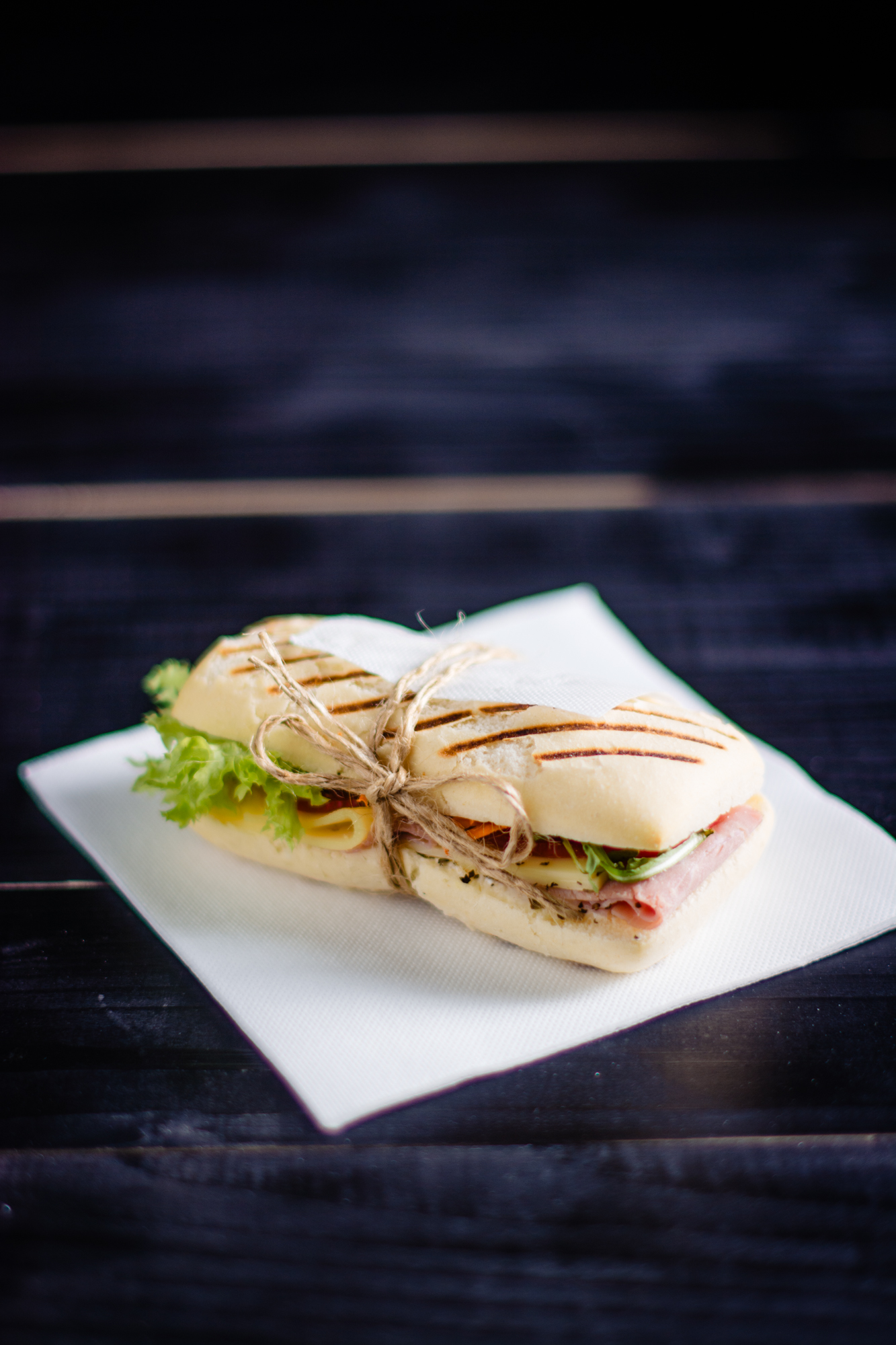 Grilled sandwich tied with twine, filled with cheese and ham on textured dark surface.
