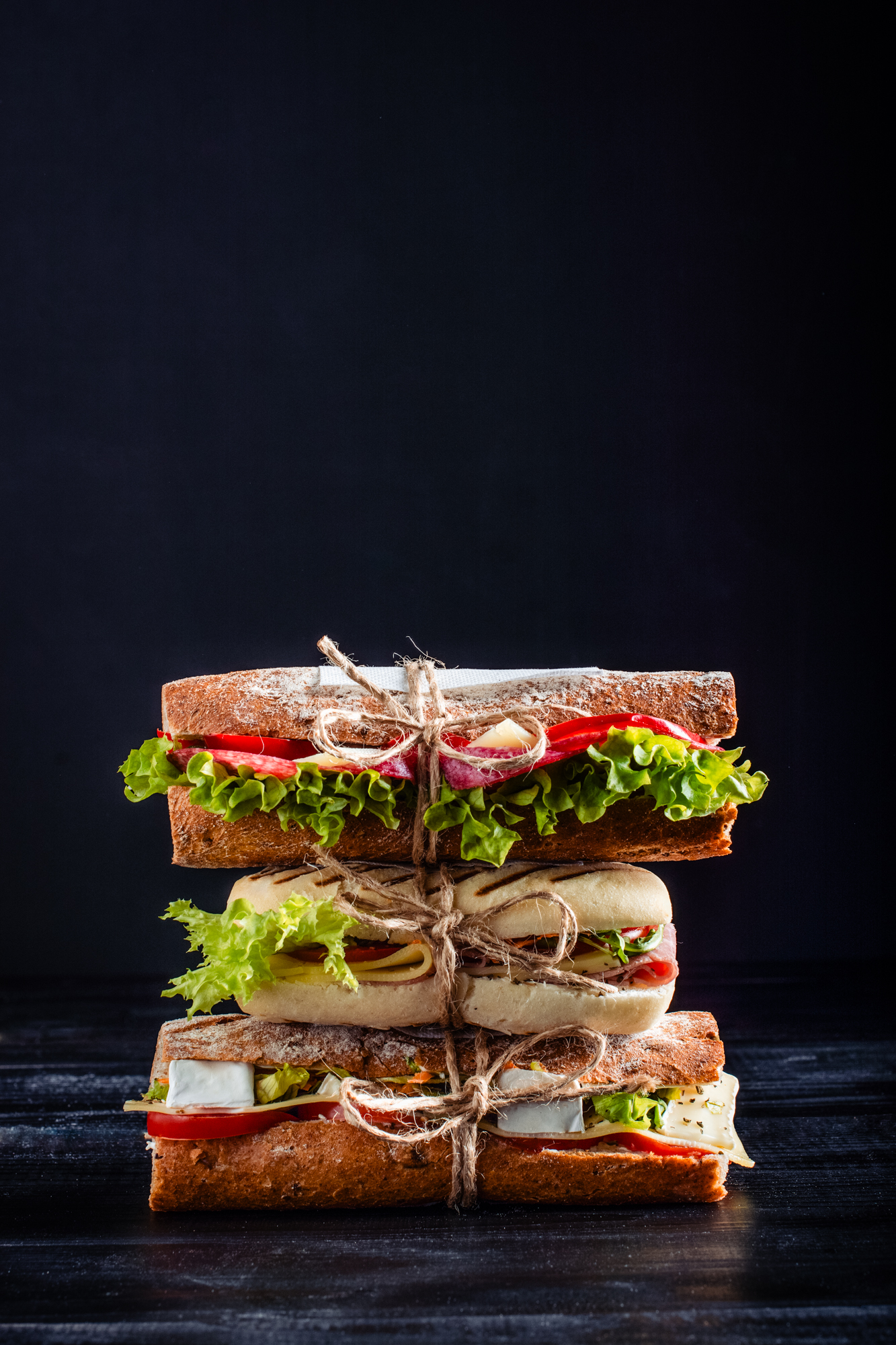 Stacked artisan sandwiches tied with string, showcasing layered fillings in bakery food photography.