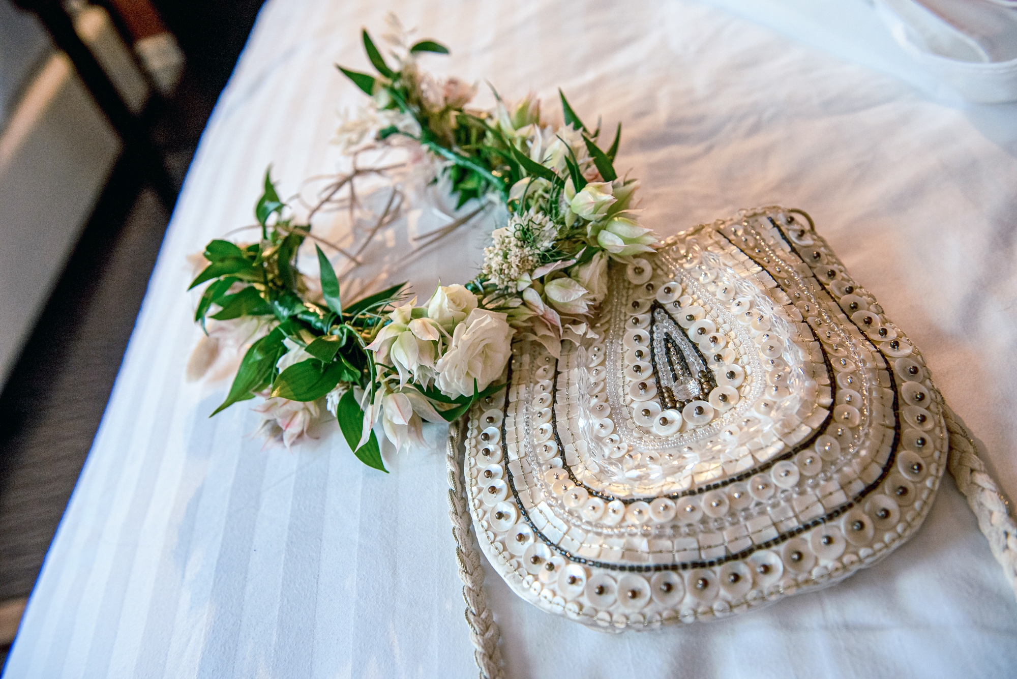 Floral crown and beaded bridal bag laid on bed during wedding preparations.