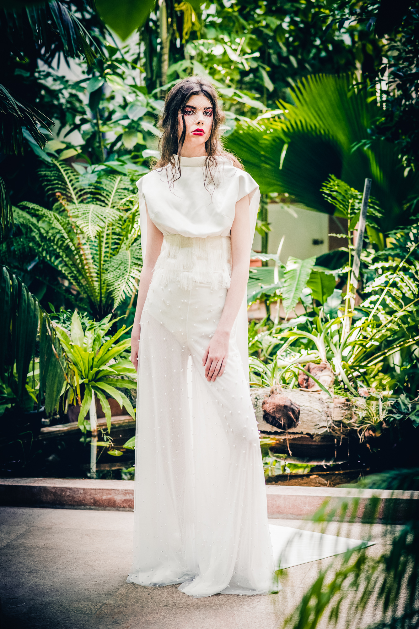 Full-length bridal editorial shot with long train surrounded by lush greenhouse plants.