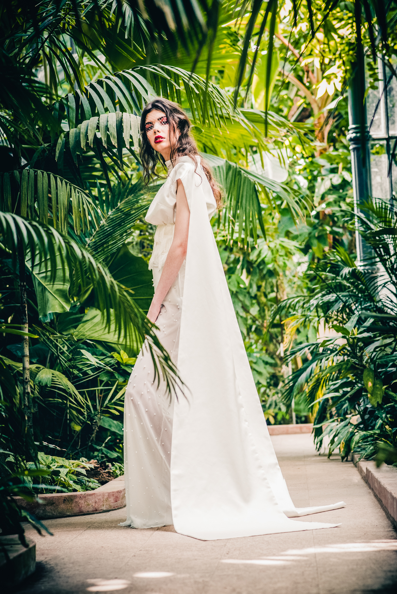 Bride in modern white dress posing between palm leaves in botanical garden Budapest.