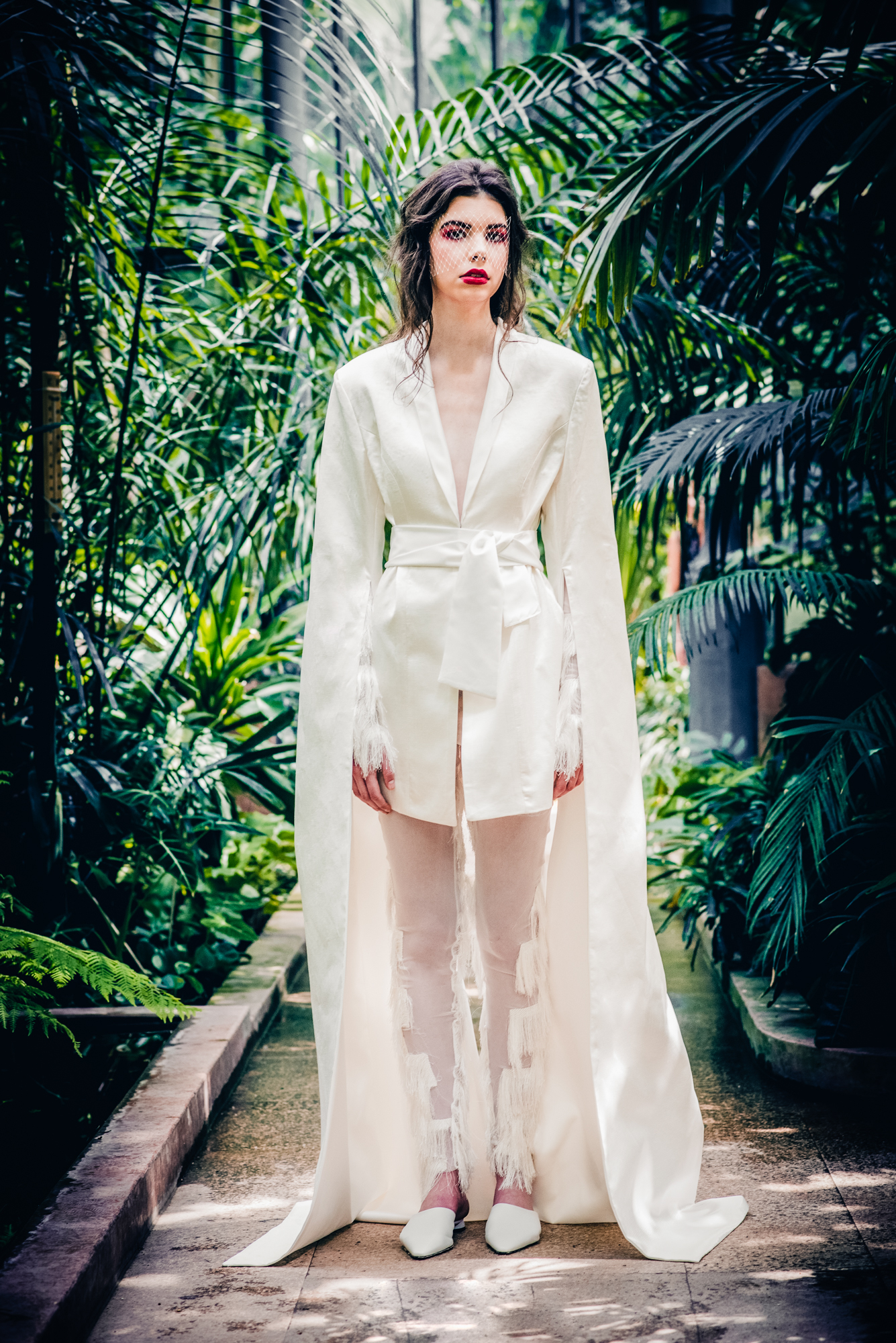 Bridal editorial portrait in botanical garden with white structured outfit and tropical plants.