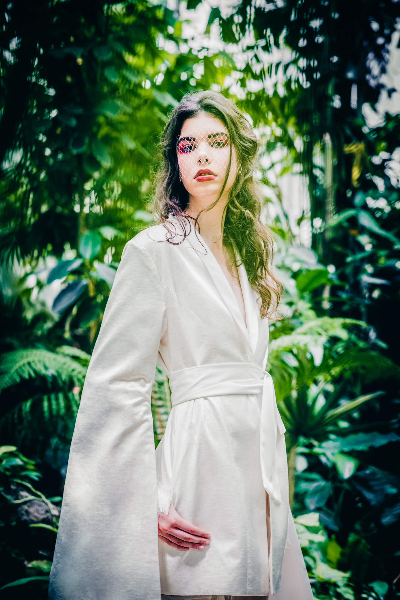 Bridal portrait with soft veil detail and greenery background in botanical garden editorial shoot.