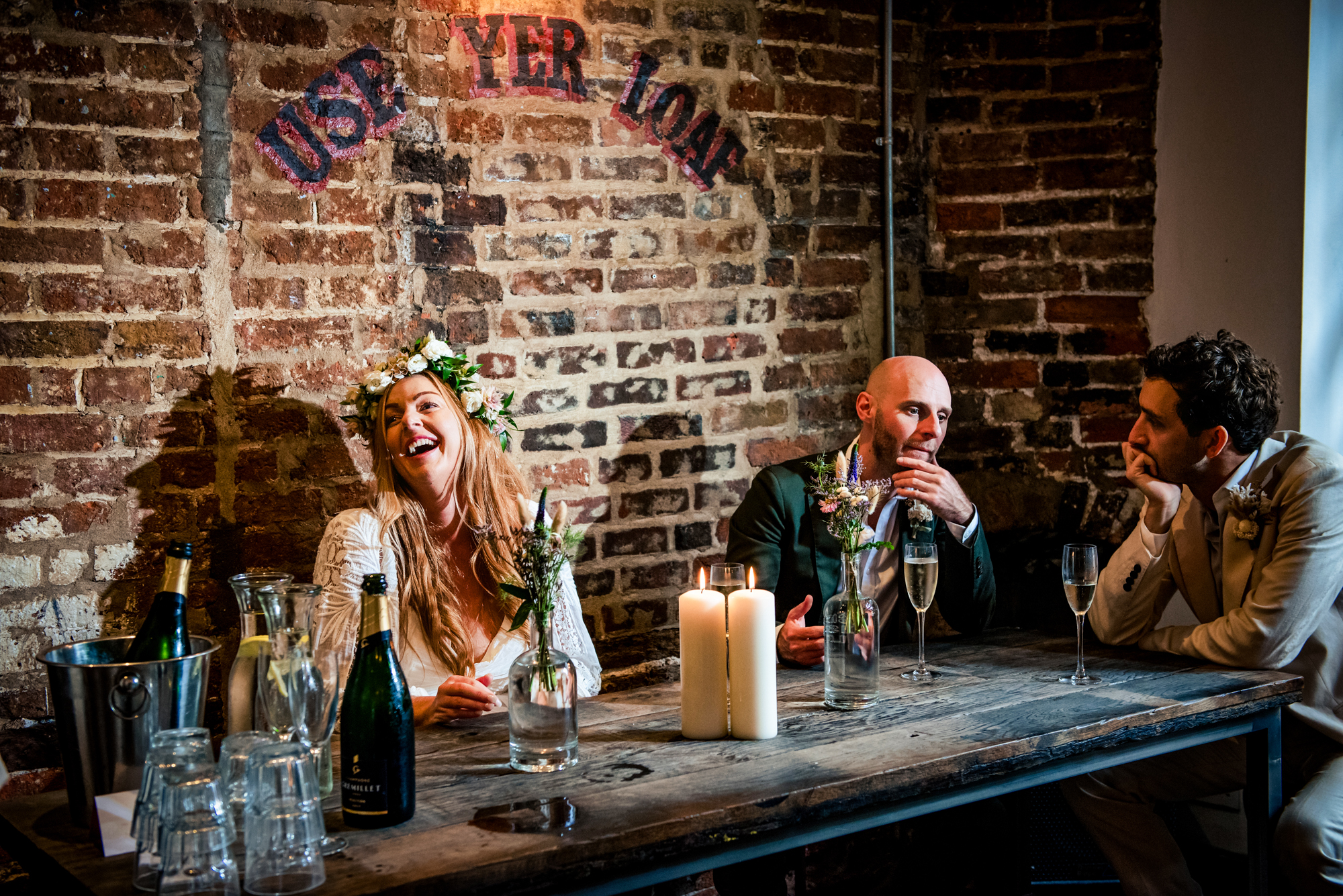 Bride laughing at table with groom and friends during lively reception moment.