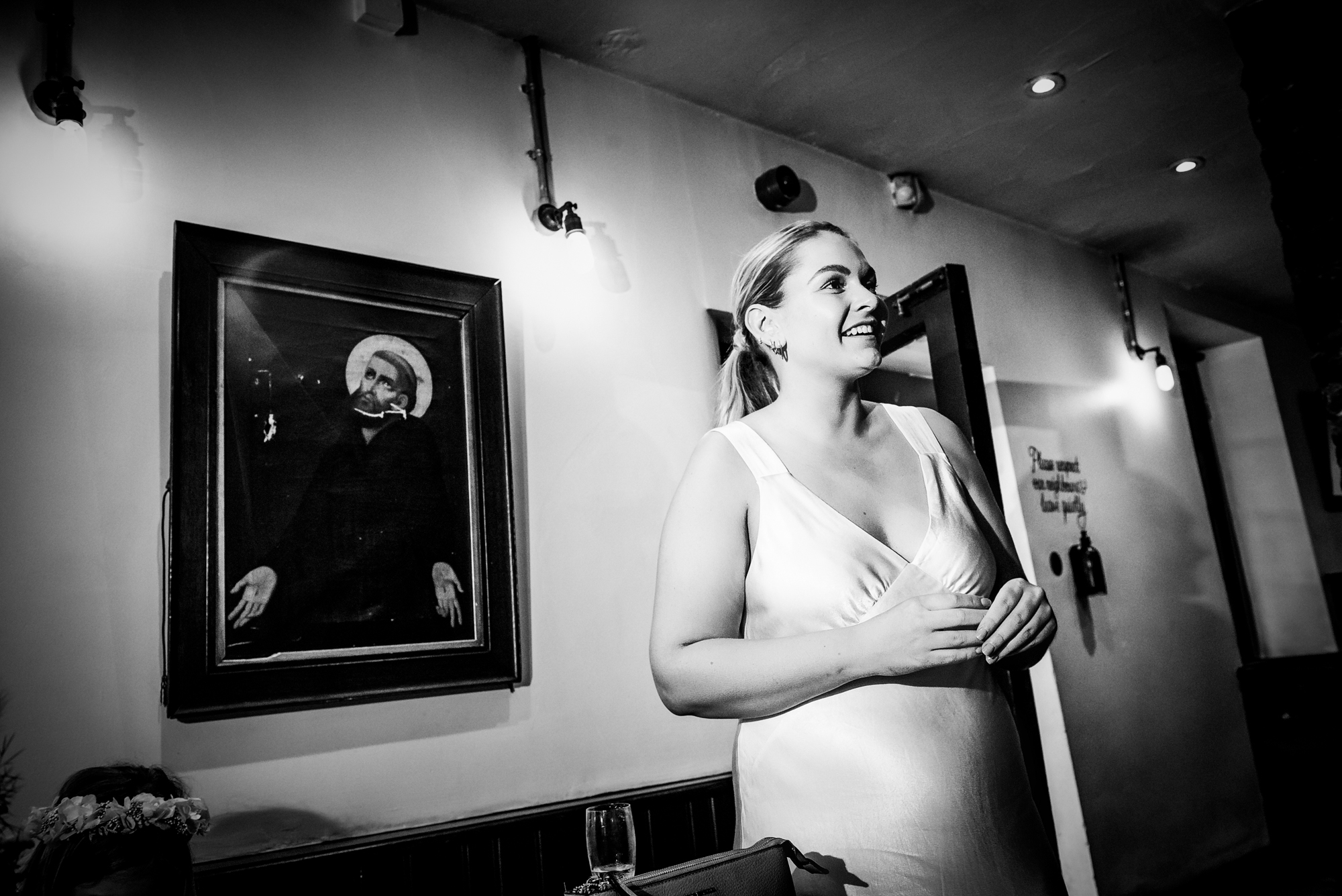 Woman standing near wall with framed artwork in quiet candid reception moment.