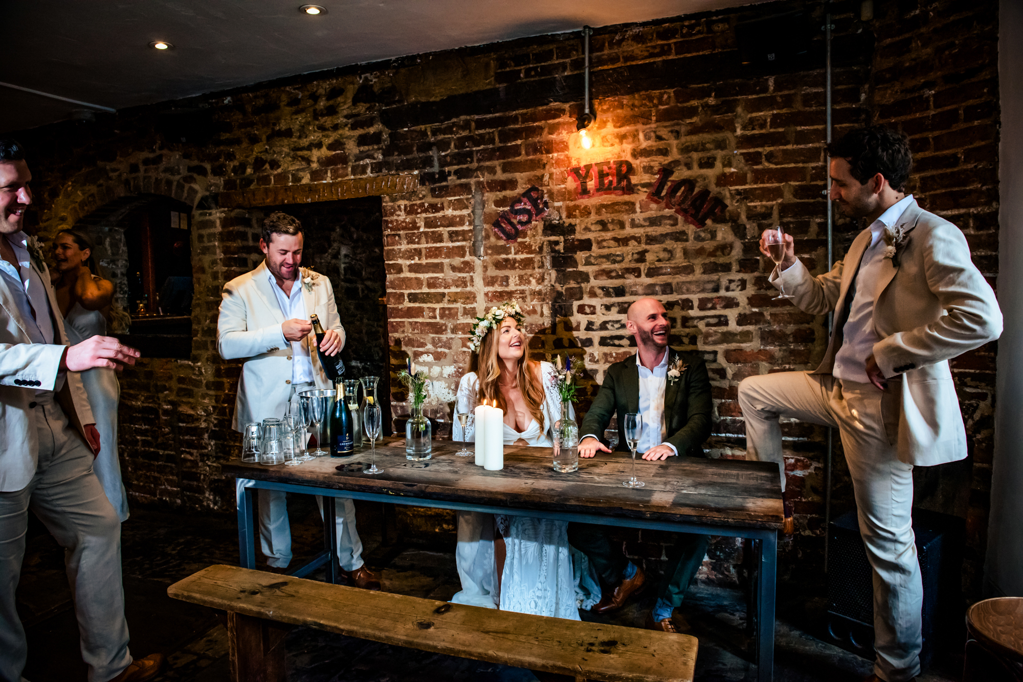 Group of guests chatting and laughing around table during evening wedding reception.