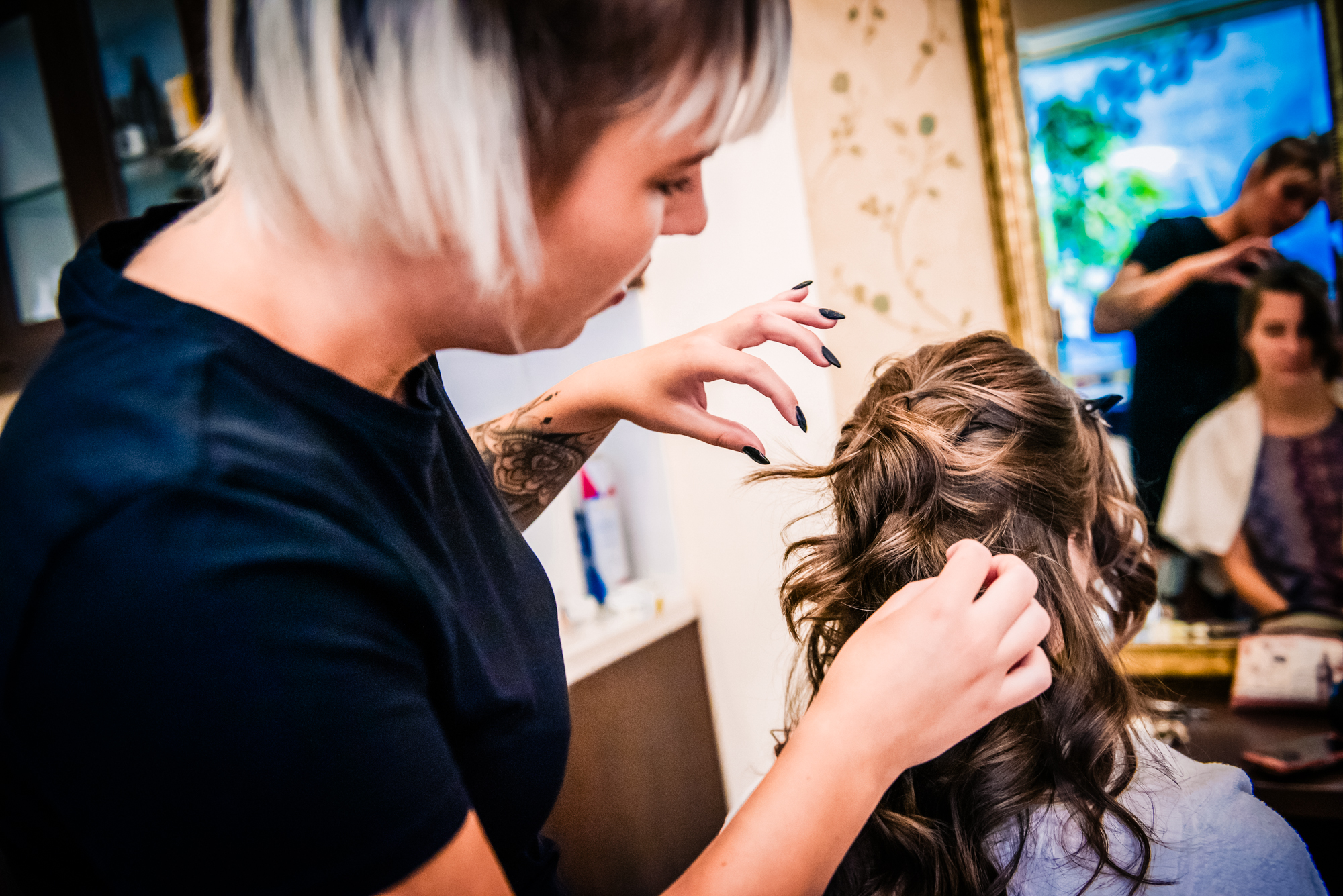 Hairstylist curling woman’s hair during bridal-style preparations before family christening celebration.