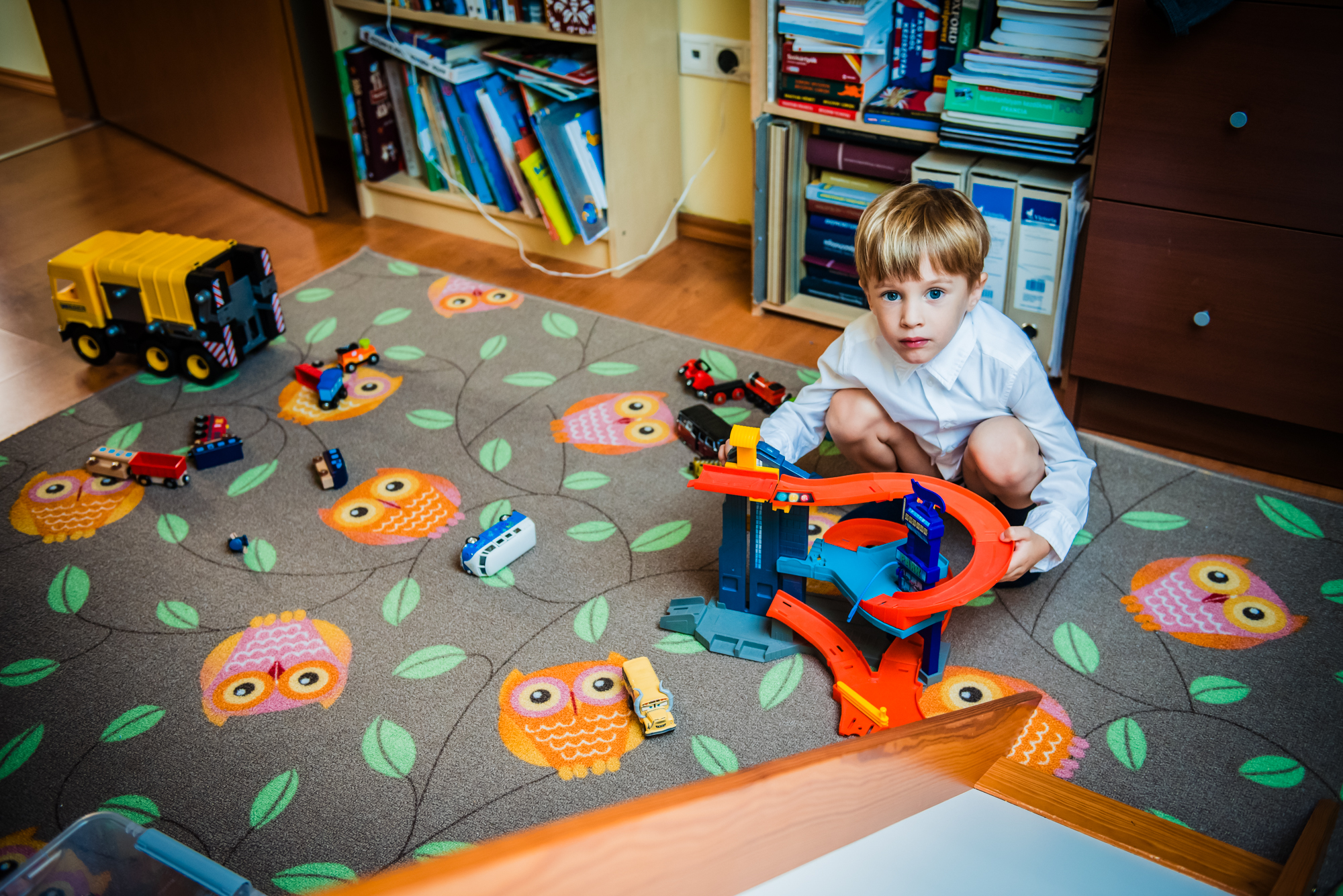 Young boy playing with toy cars on an owl-pattern rug before his christening ceremony.