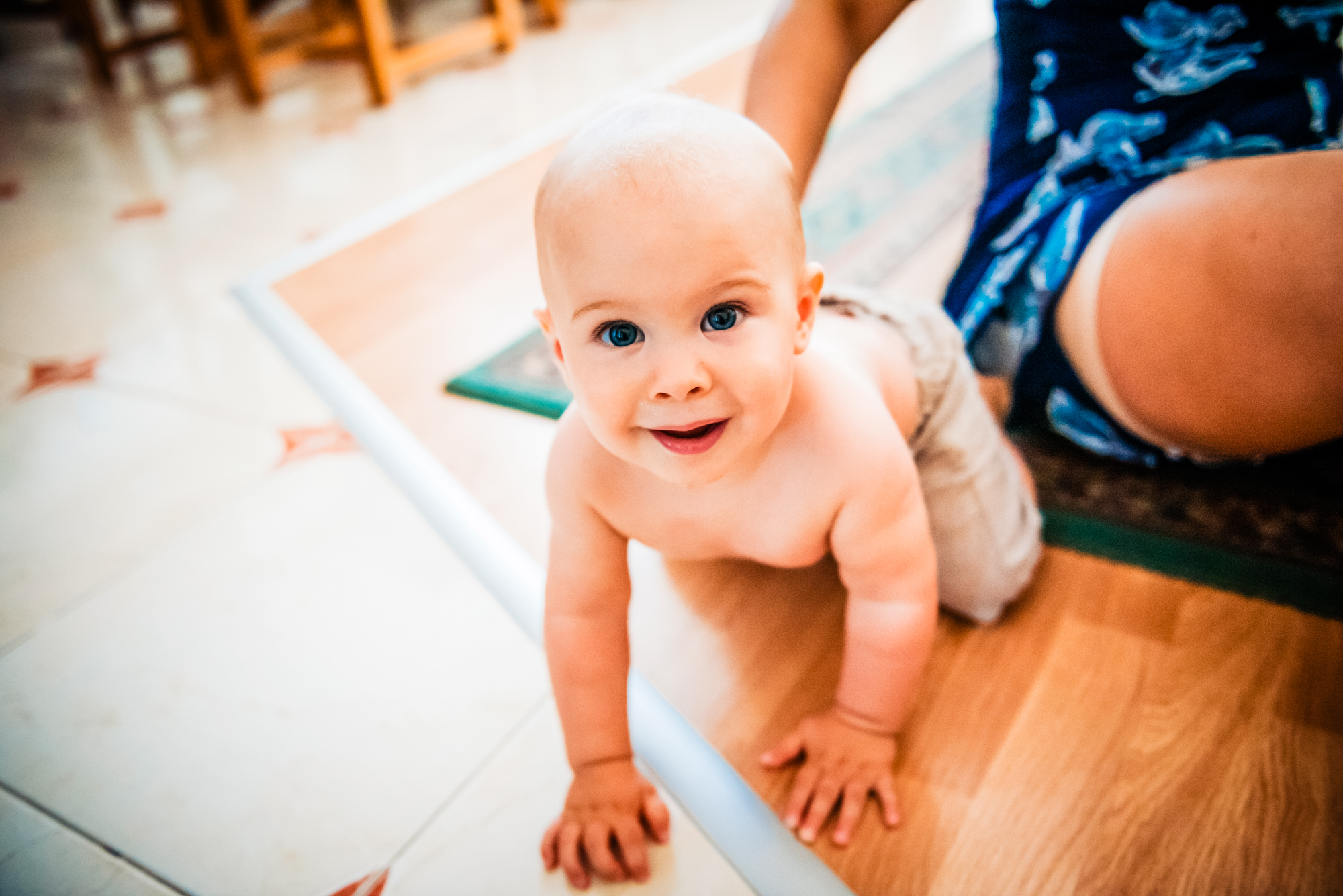 Crawling baby smiling at the camera on a wooden floor before the christening ceremony.