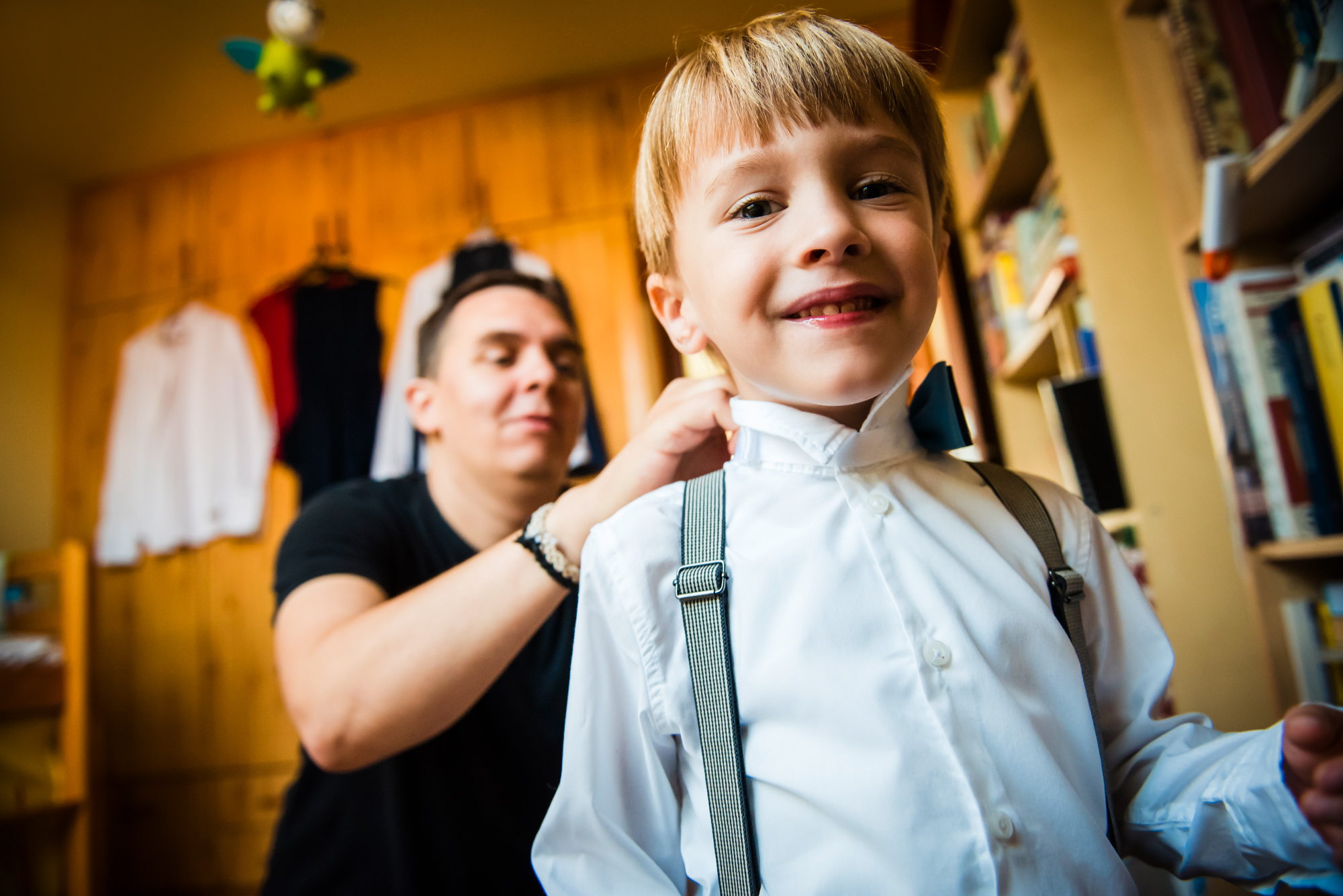 Smiling little boy wearing suspenders and bow tie while getting ready for a christening.