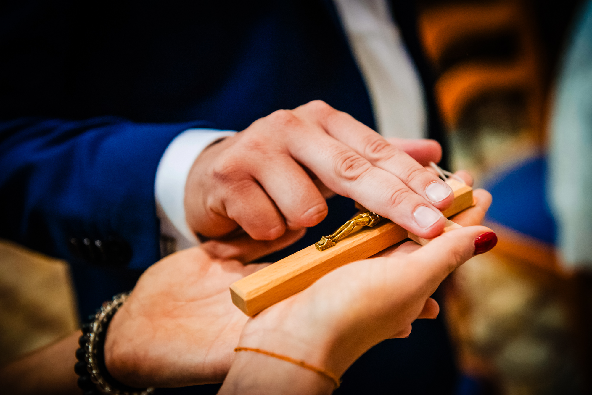 Hands holding a wooden crucifix during a Catholic christening ritual.