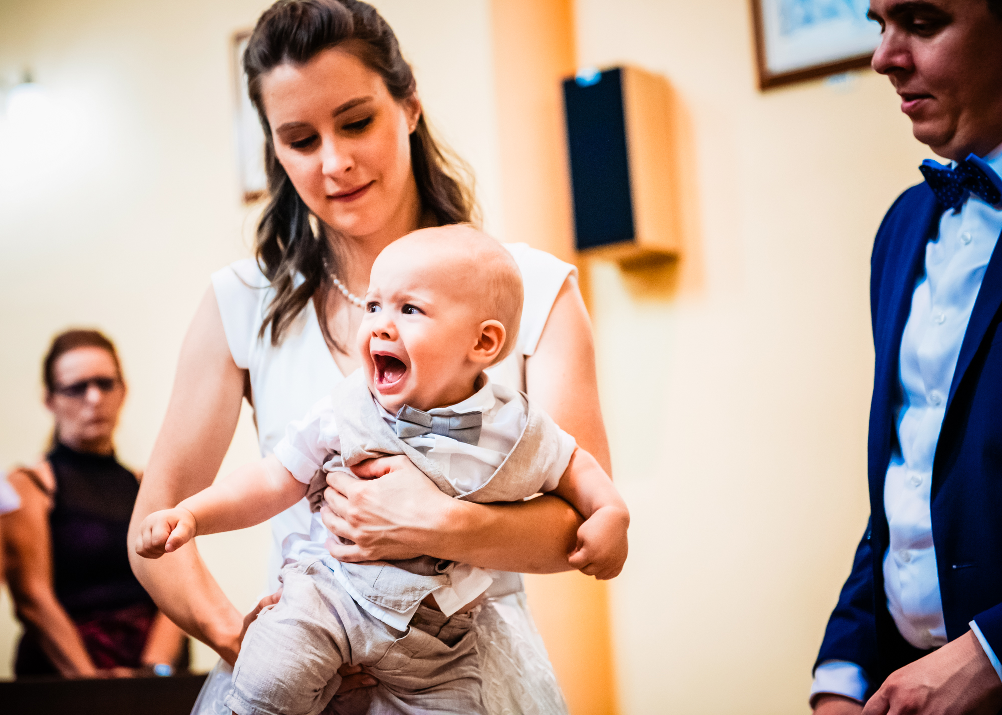 Baby crying in mother’s arms during emotional christening ceremony inside warm church light.