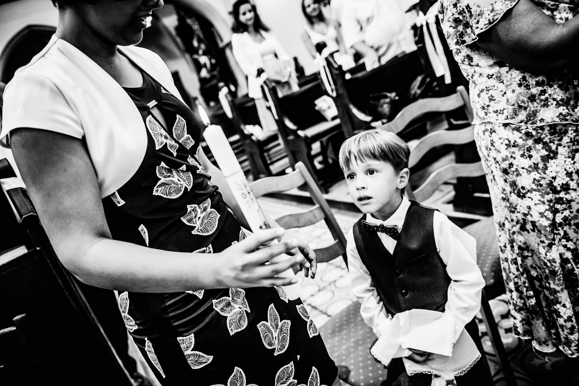 Little boy holding christening candle while standing beside family during church ceremony.