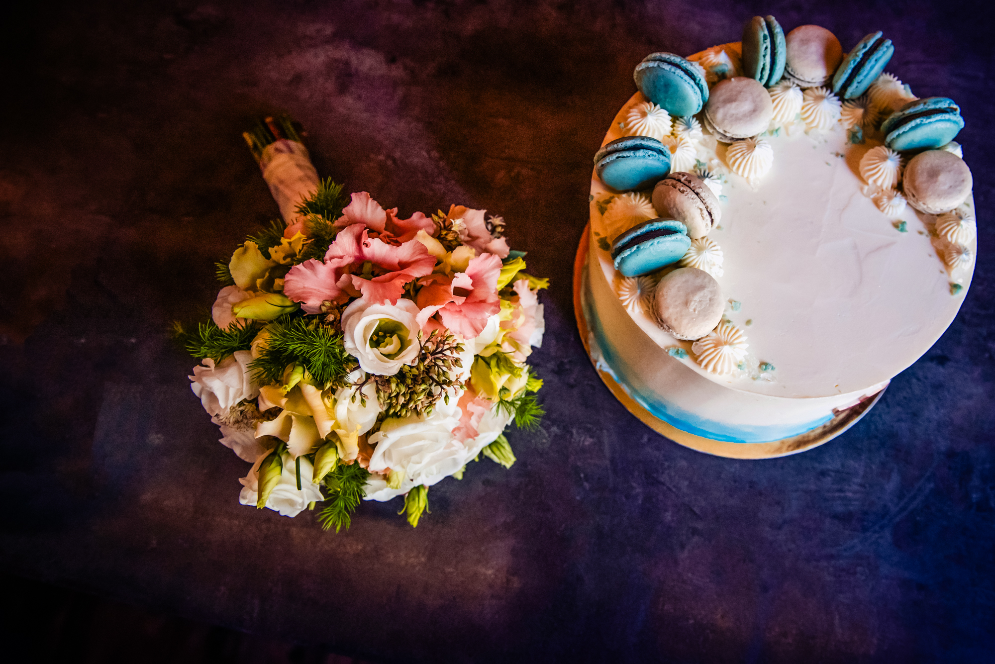 Overhead view of christening cake and pastel flower bouquet on dark reception table.