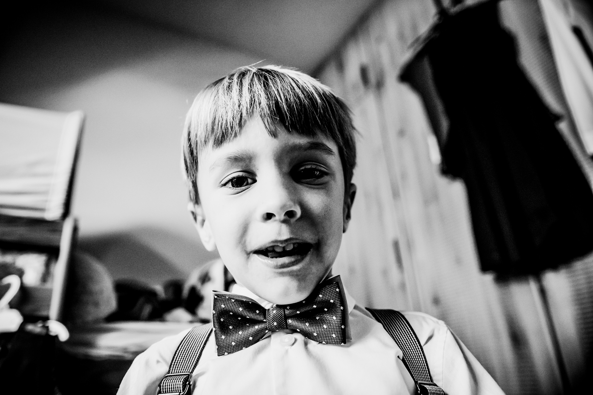 Black and white portrait of young boy in bow tie and suspenders before christening ceremony.