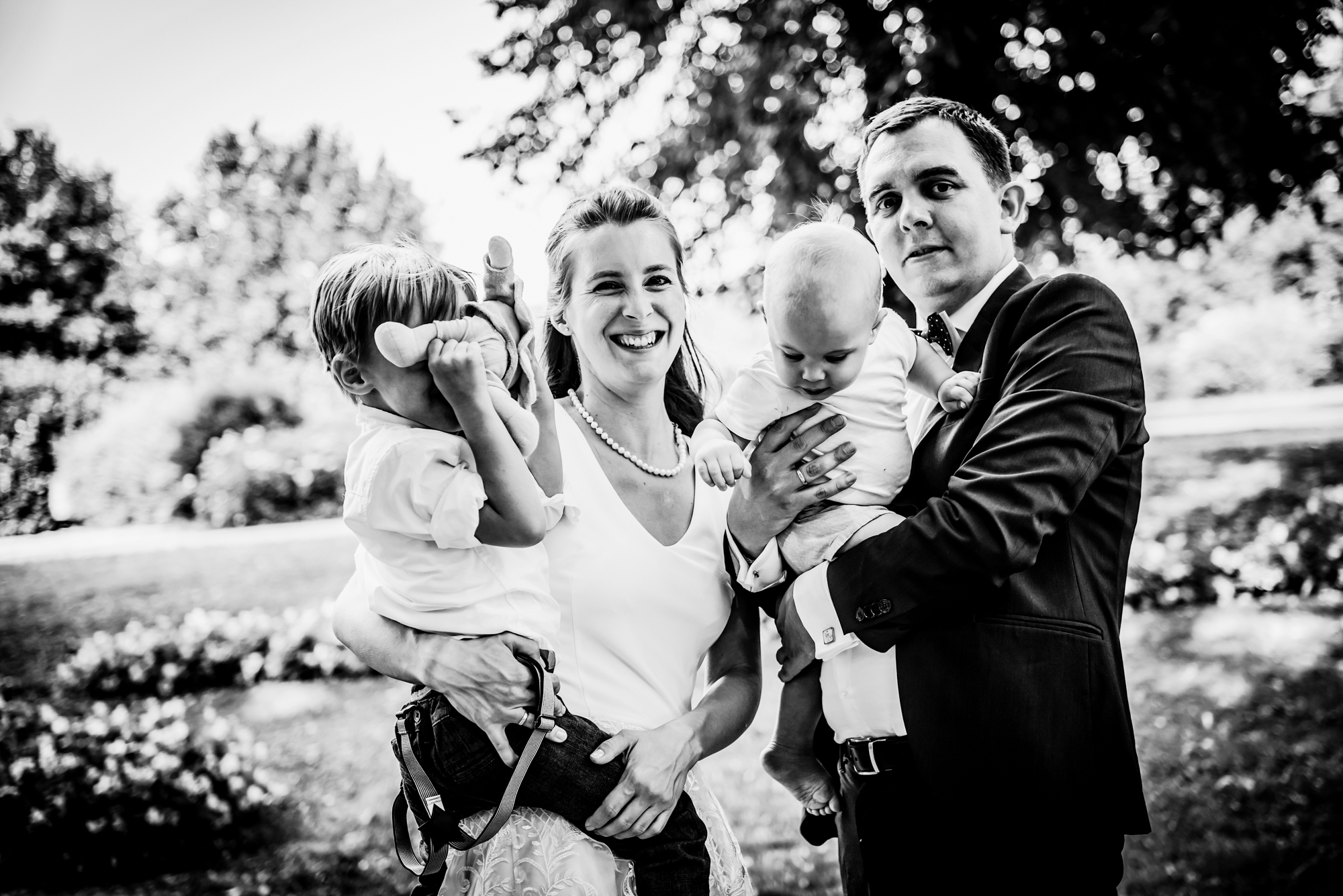 Family portrait outdoors after church christening with parents holding two young children.