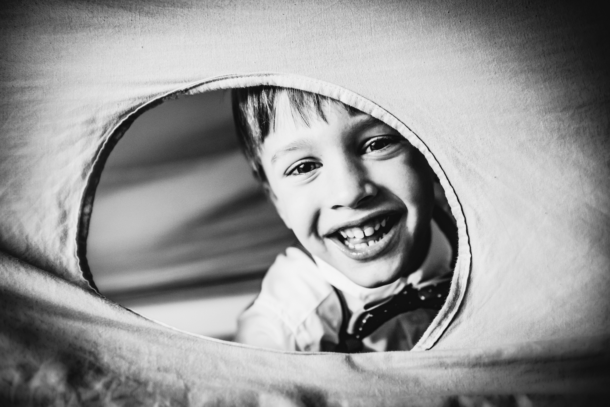 Black and white close-up of smiling boy inside a play tunnel before family celebration.