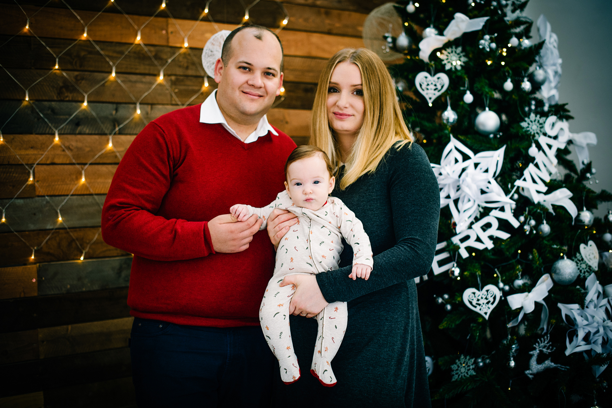 Parents hold baby Bella in front of a Christmas tree during a festive family session.