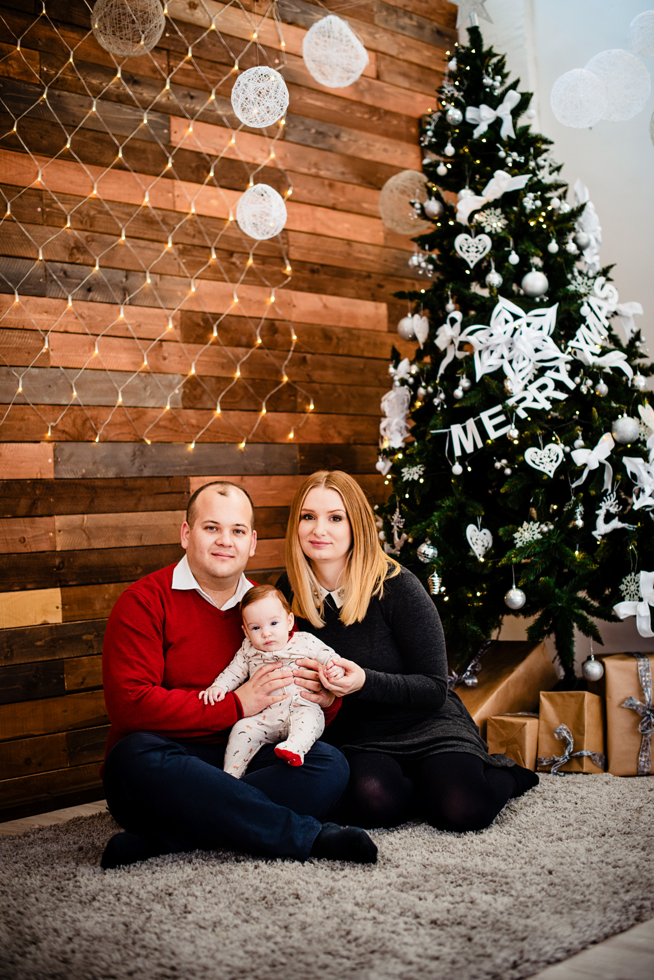 Family sits together beside a Christmas tree during a warm Christmas studio photo session.
