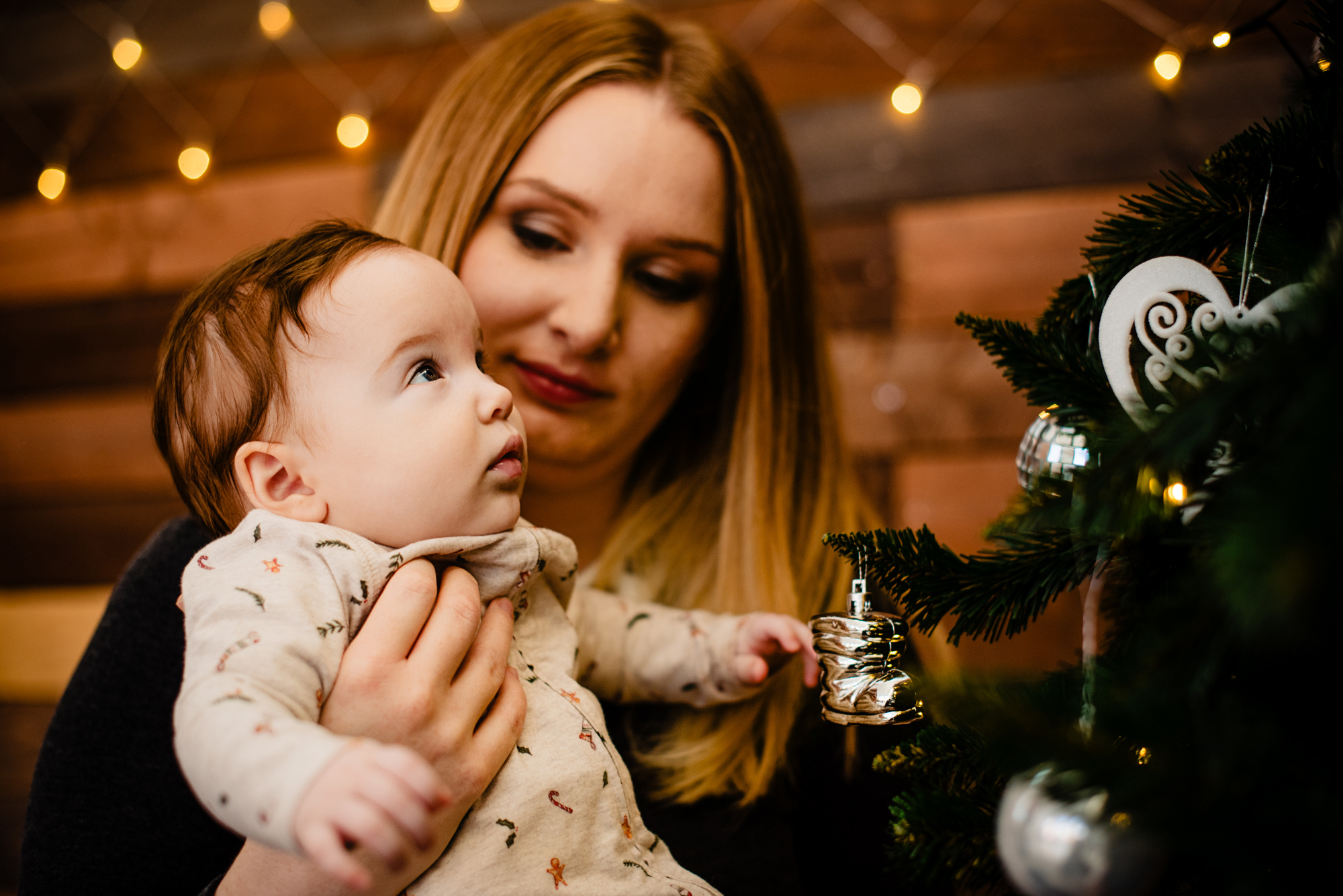 Mother holds baby Bella close while they look at Christmas tree decorations in the studio.