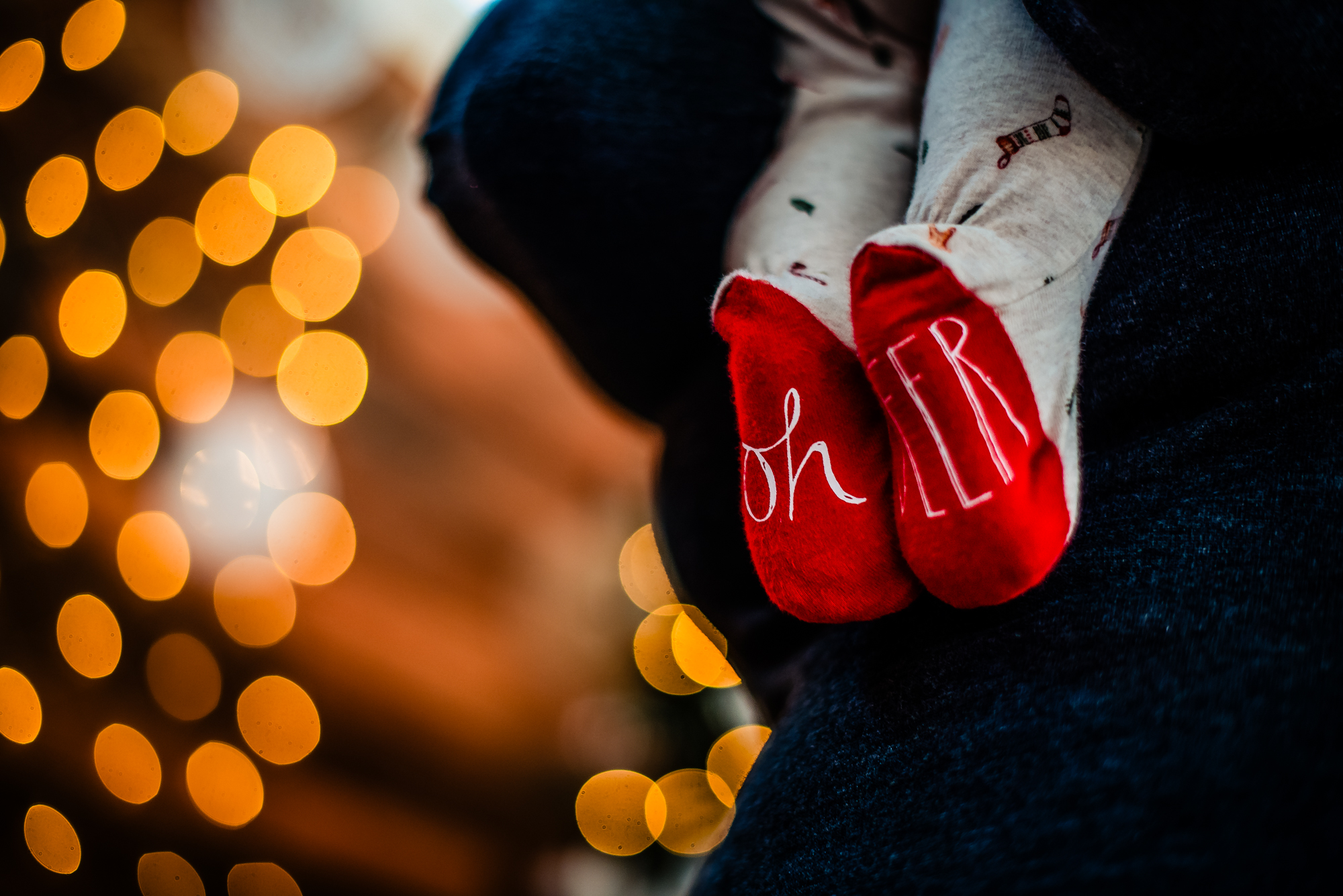 Close-up of baby Bella’s red Christmas socks against warm golden studio lights.