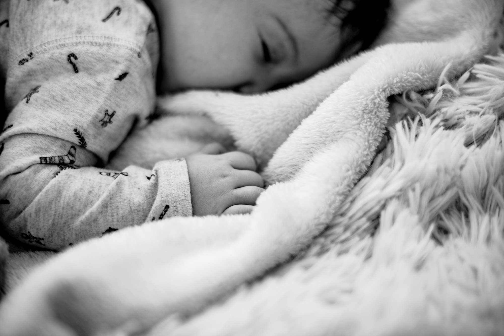 Black and white detail of baby Bella resting with hand tucked into a soft blanket.