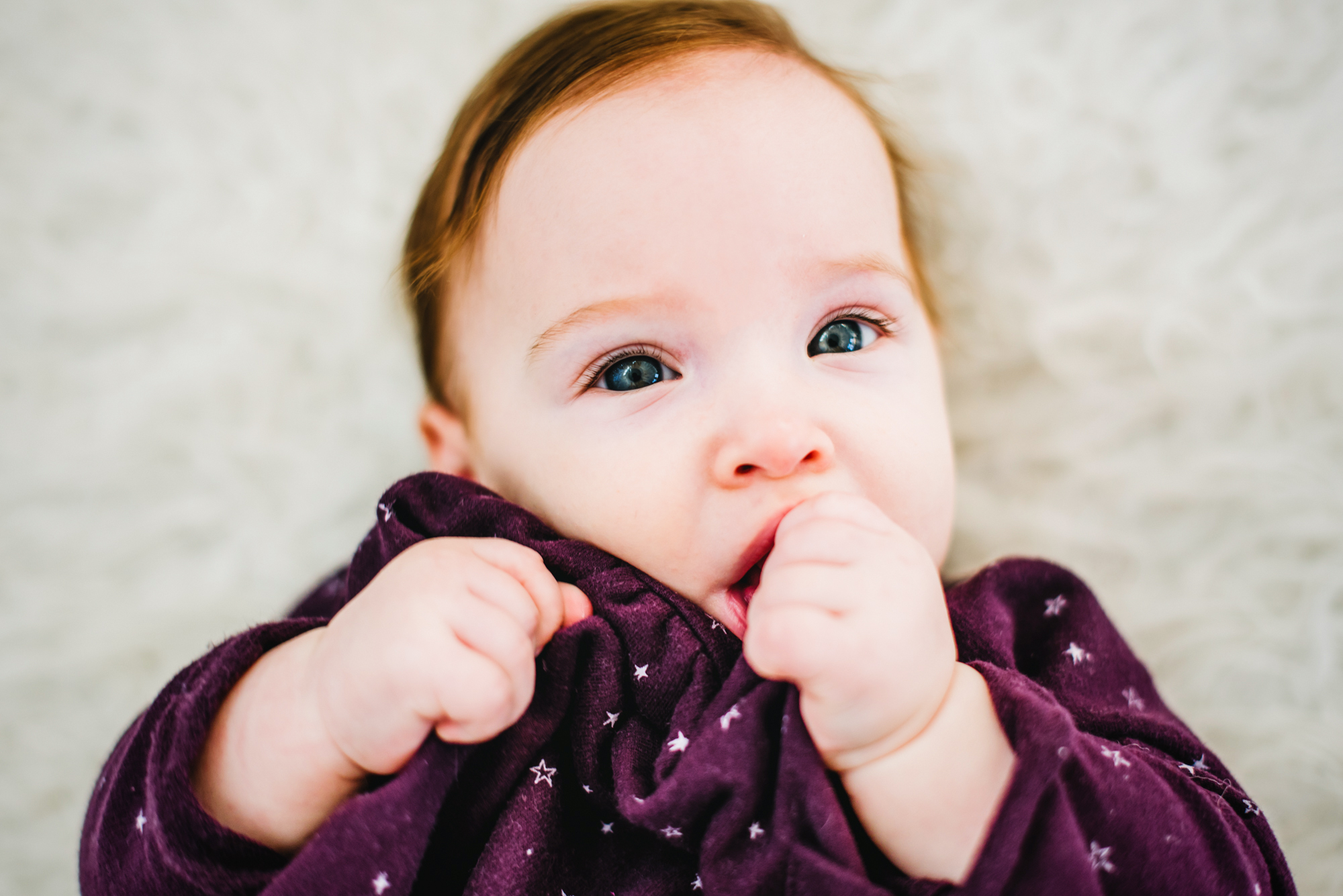 Baby Bella holds her dress near her mouth during a Christmas baby studio session.