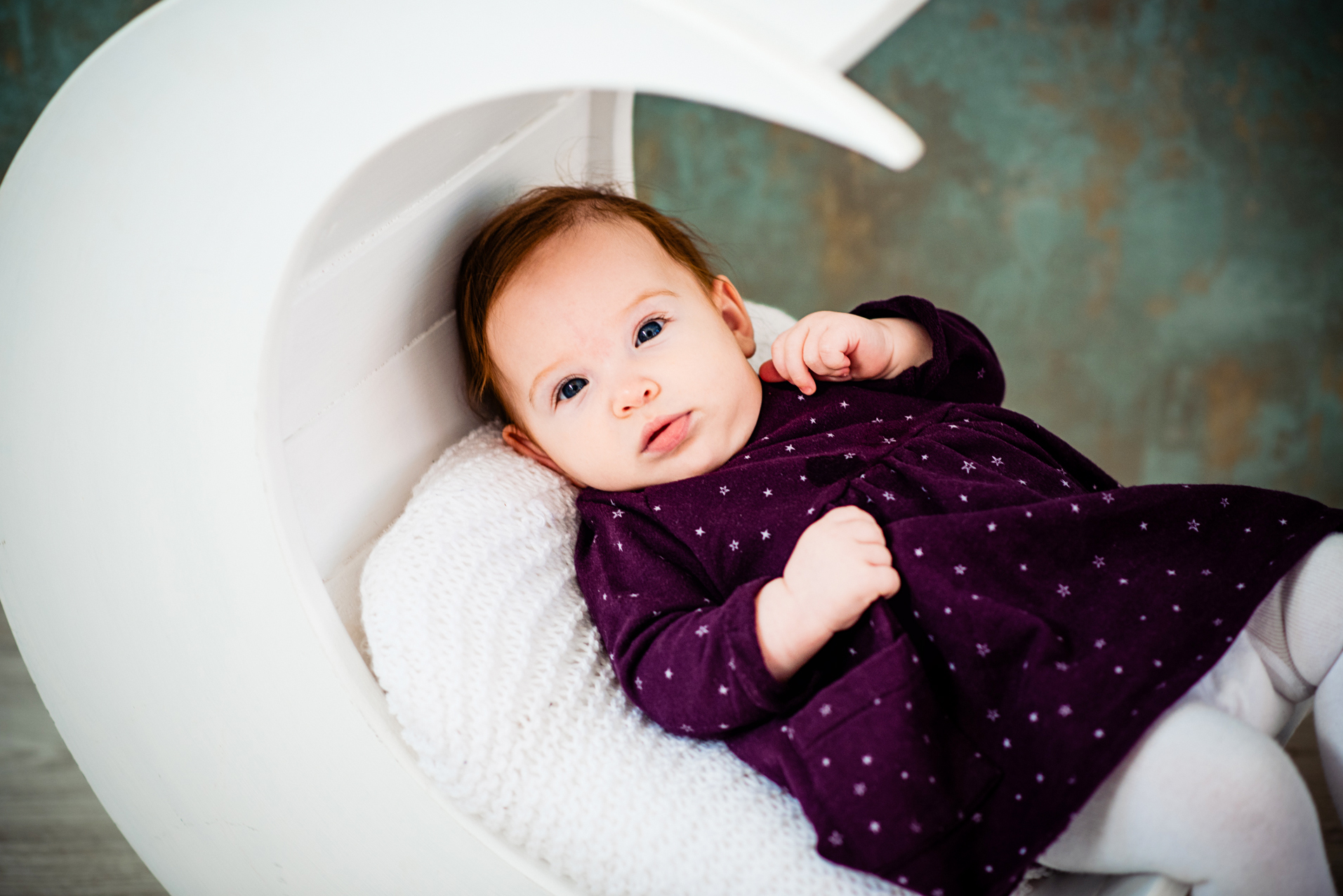 Baby Bella rests in a white crescent moon prop during a Christmas studio session.