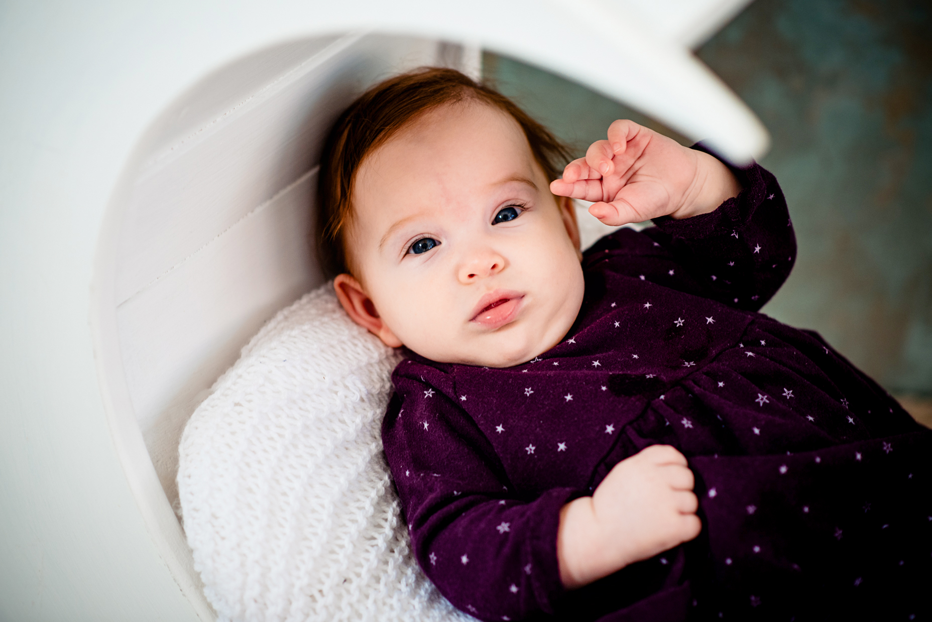 Baby Bella lies in a crescent moon prop wearing a dark purple dress and white tights.