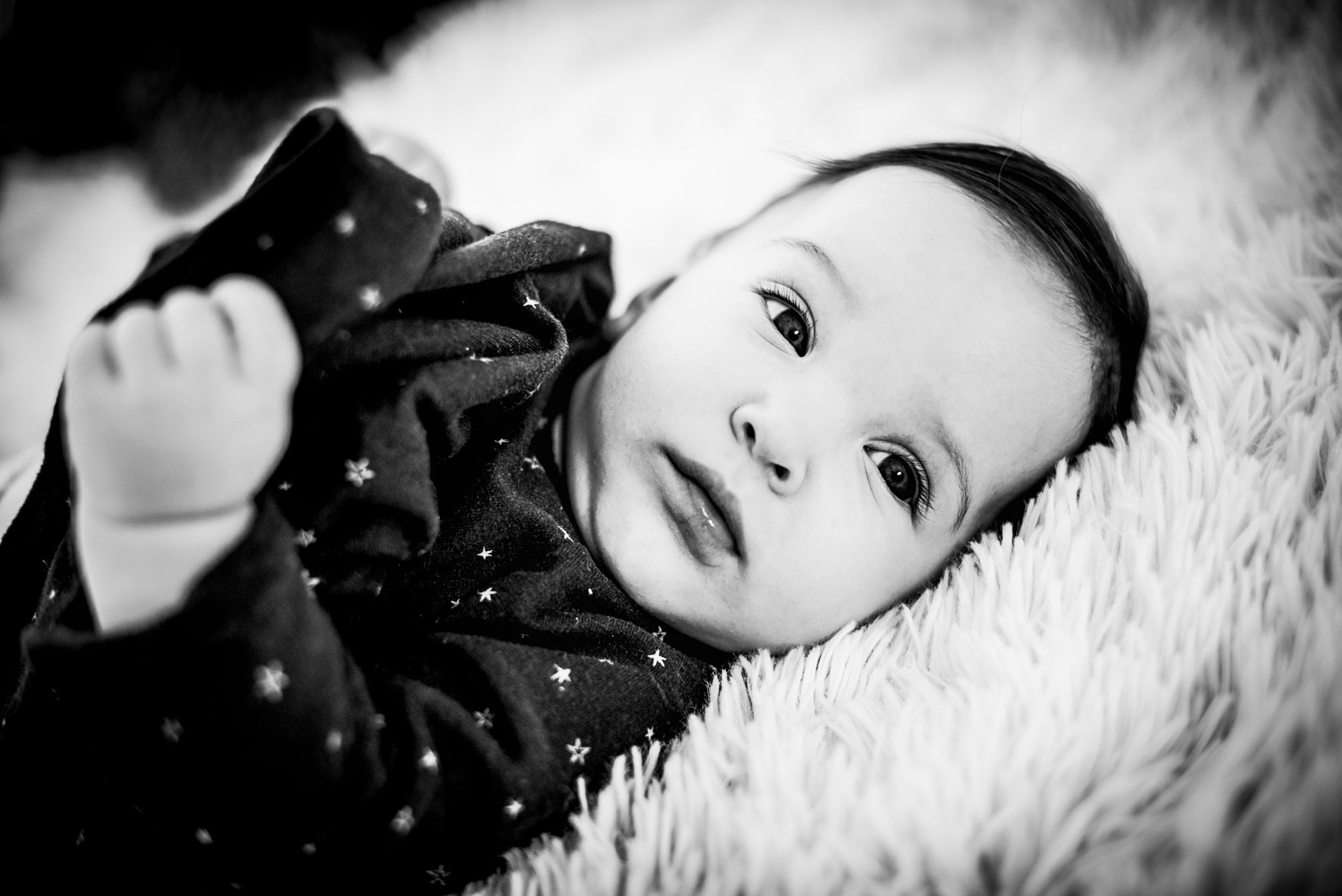 Black and white close-up of baby Bella lying on a fluffy rug in studio.