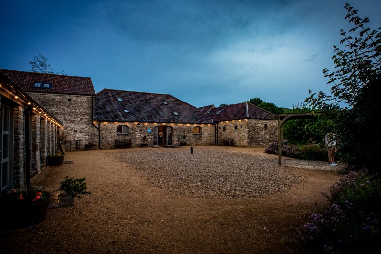Fairy lights glow across the Folly Farm courtyard at blue hour, creating a warm, welcoming evening atmosphere.