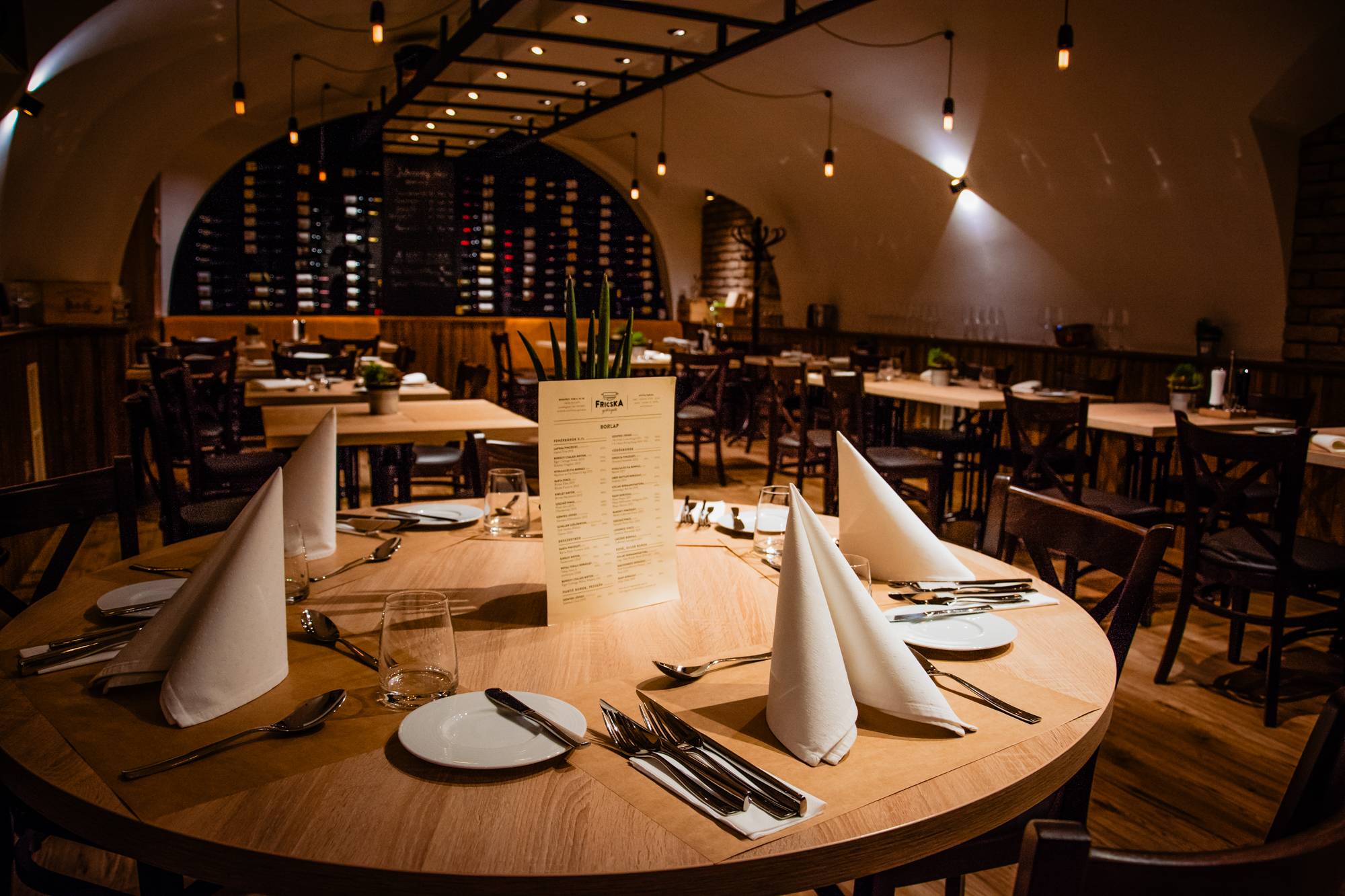 Round wooden dining table set for dinner inside Fricska Gastropub wine cellar restaurant.