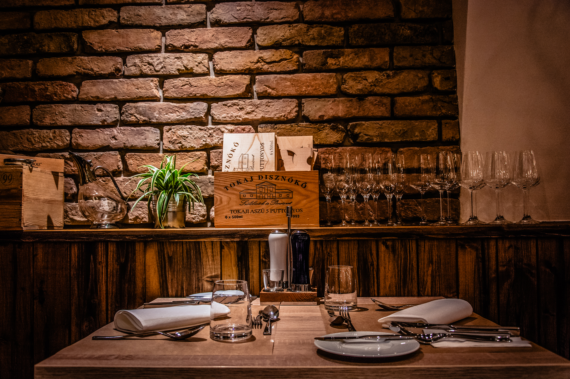 Wooden dining table with wine glasses and exposed brick wall inside Budapest gastropub.