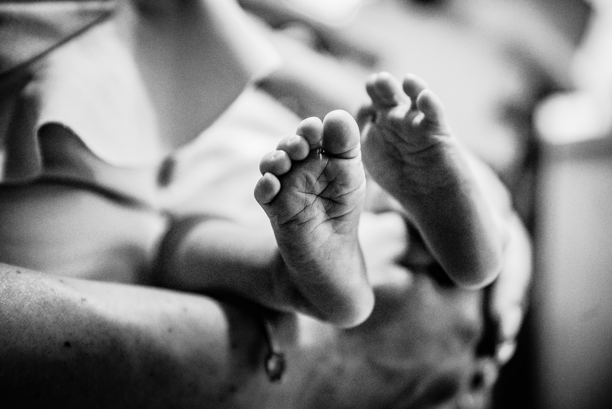 Black and white close-up of newborn baby feet held gently during intimate family moment.