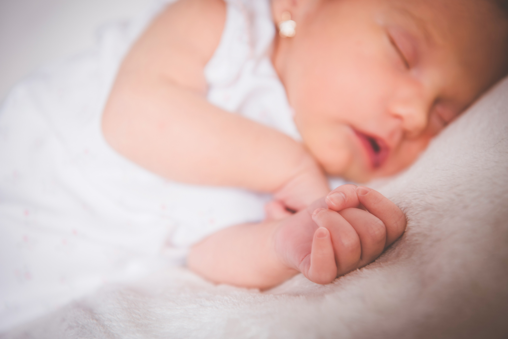 Soft focus detail of newborn baby hands in the foreground and baby in the background.