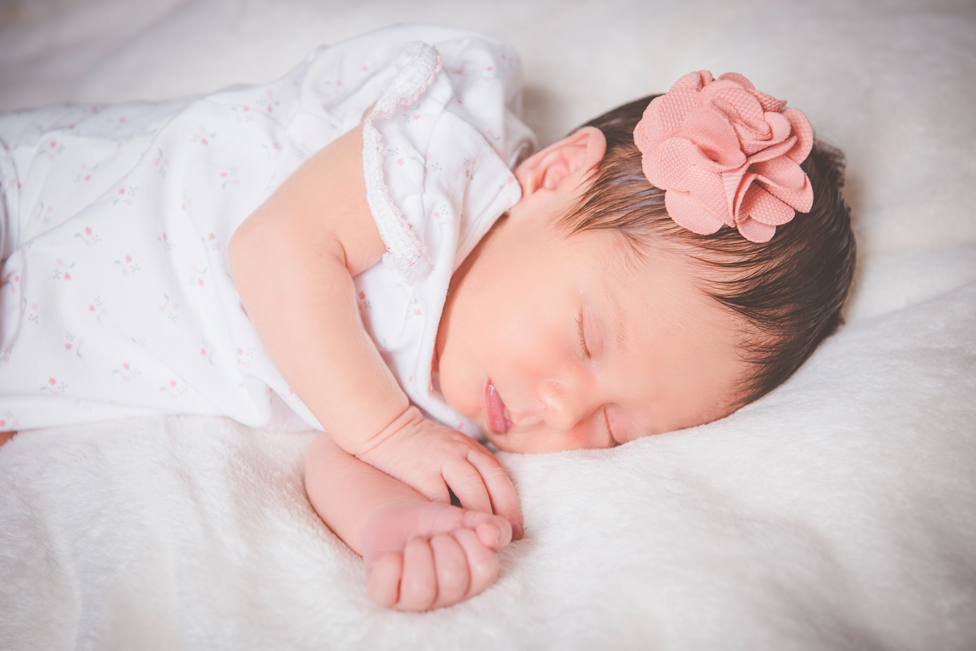 Newborn baby sleeping with hands near face on soft blanket during calm indoor session.