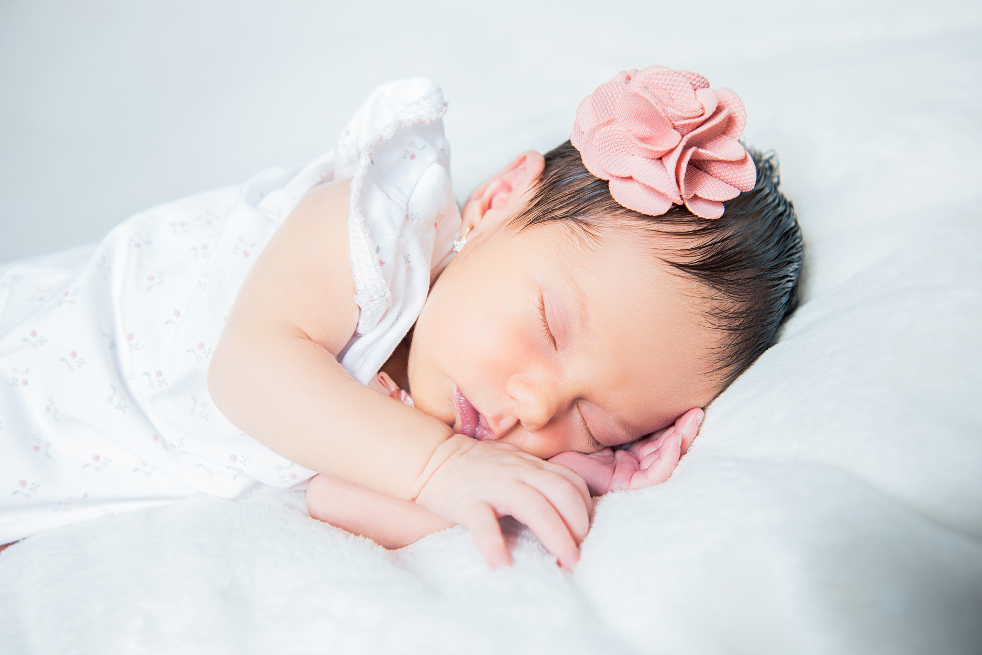 Newborn baby wearing headband, sleeping peacefully on soft surface during home session.