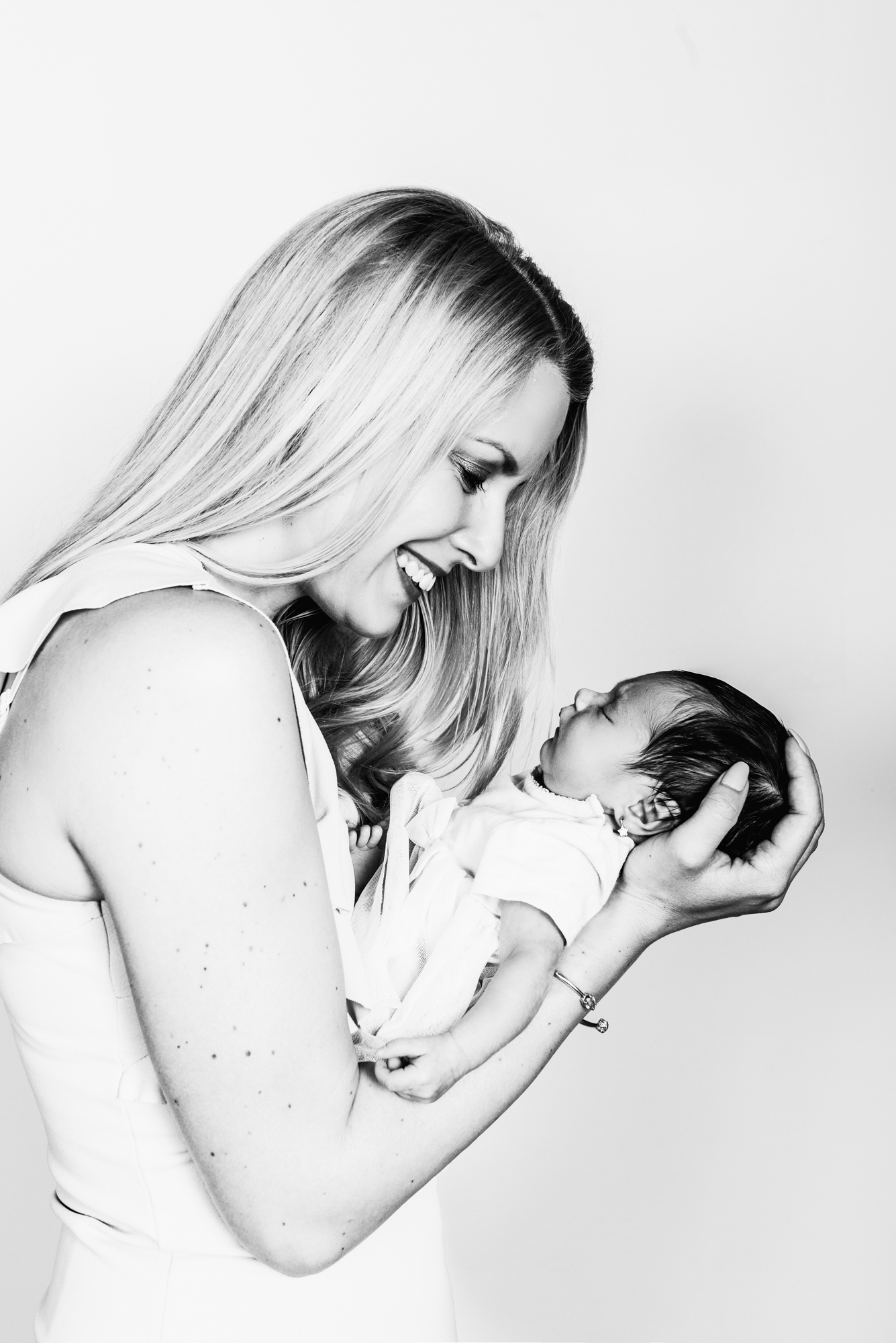 Mother holding newborn baby Kendra, smiling softly during calm indoor newborn photography session.