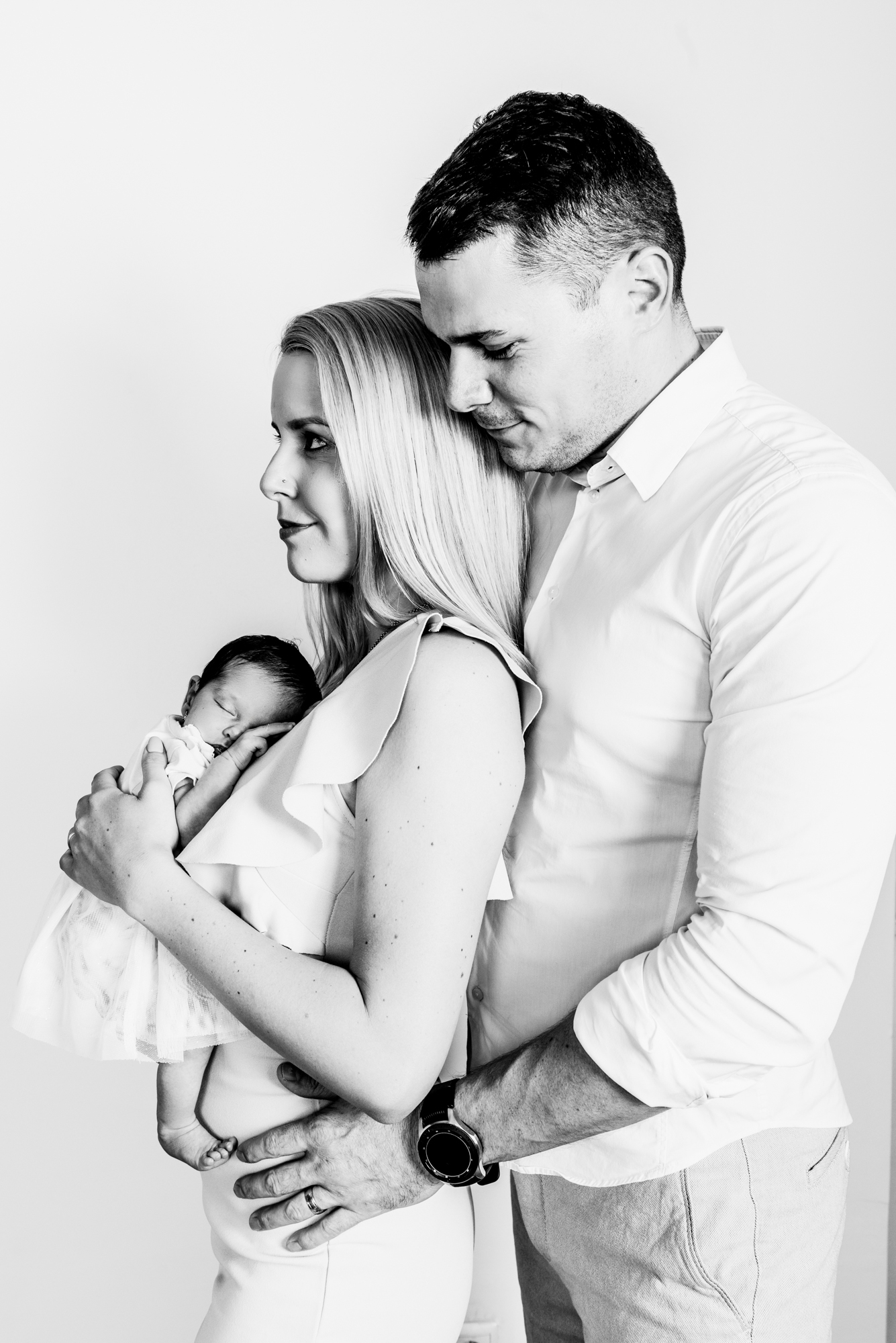 Parents embracing with newborn baby asleep in mother’s arms during peaceful home session.