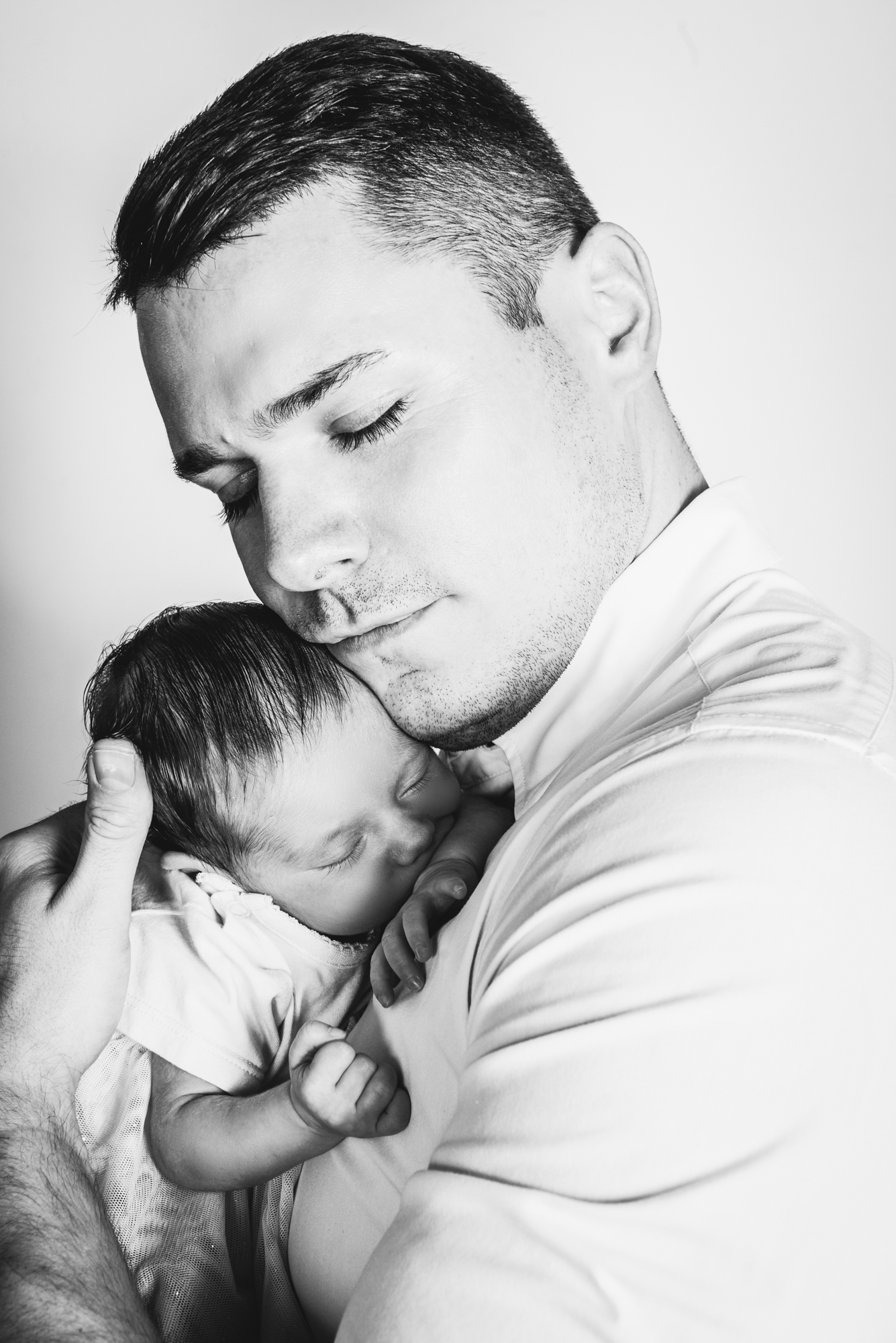 Father holding sleeping newborn baby against chest, capturing quiet bonding moment at home.