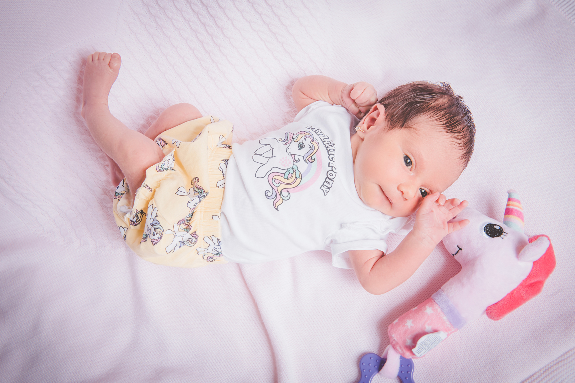 Newborn baby lying on back in outfit, looking towards camera during natural home session.